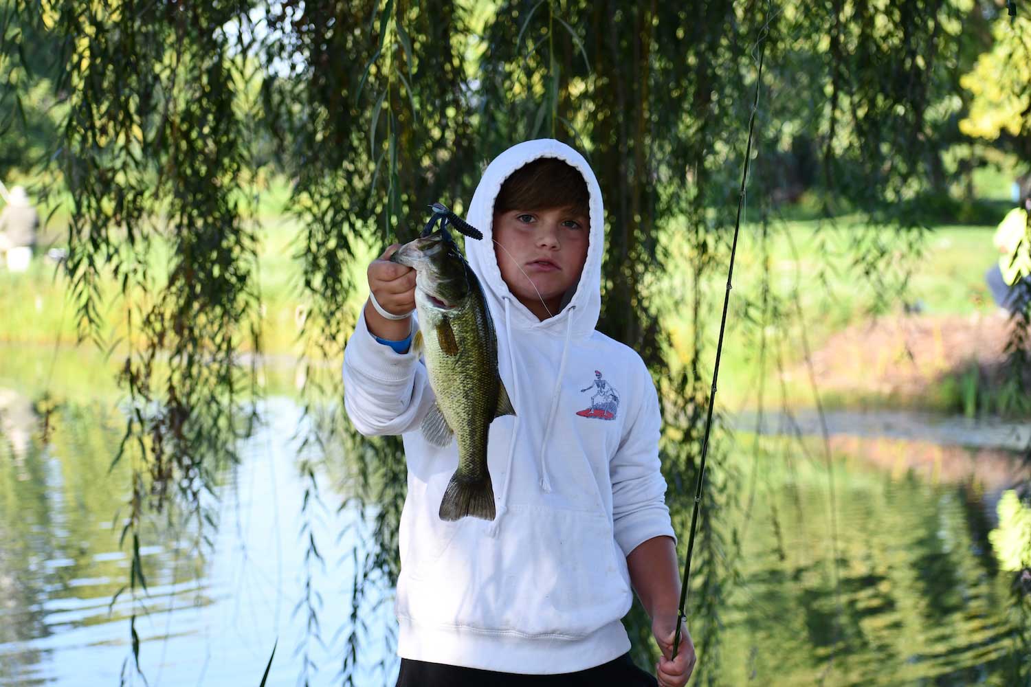 A teen holding a just caught fish in front of a lake.