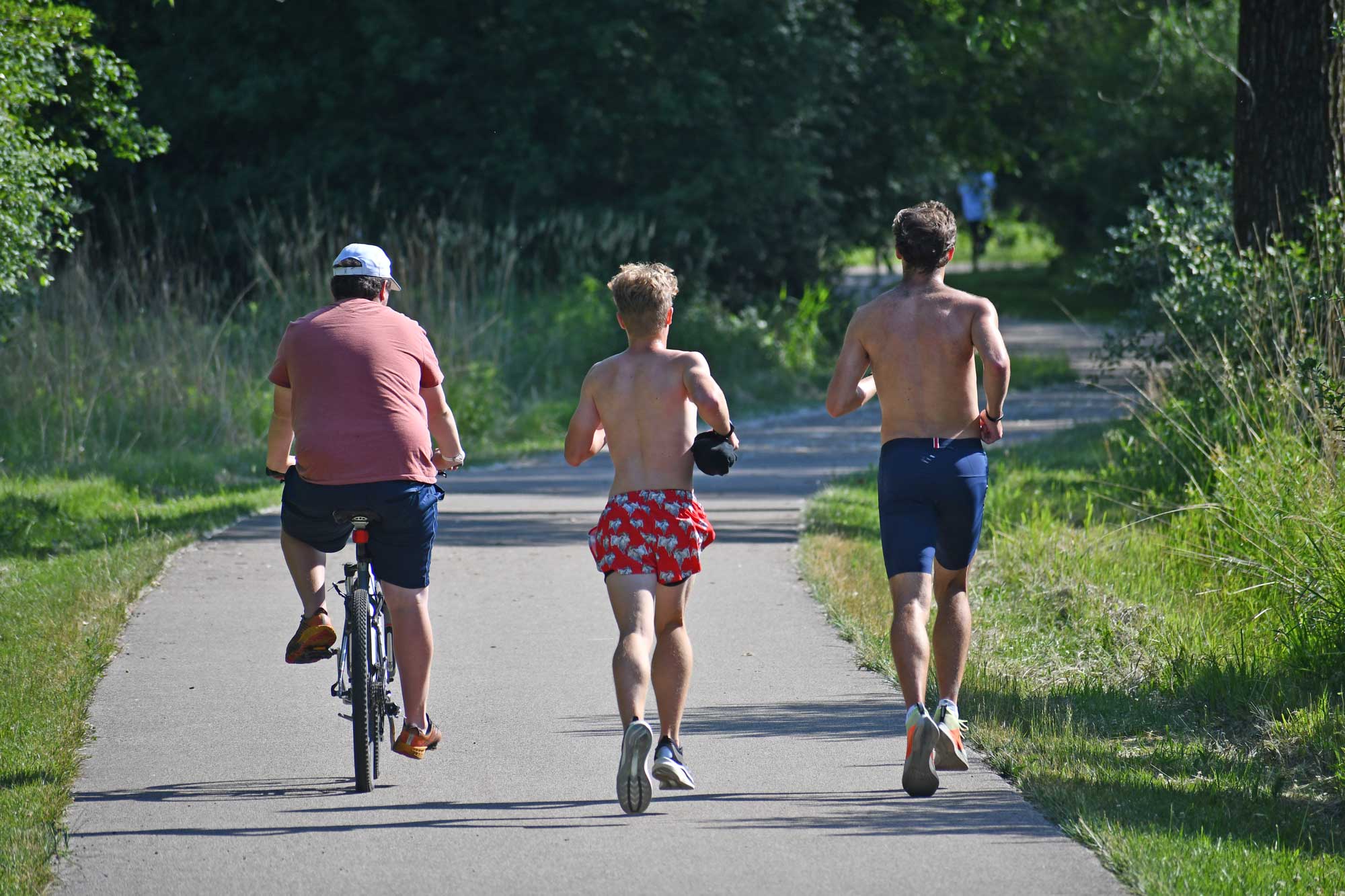 Person riding a bike and people running on a paved trail.