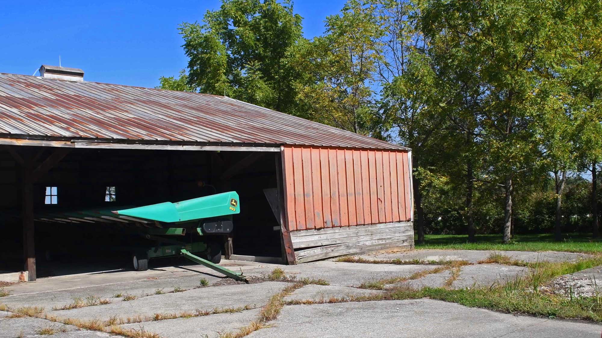Farming vehicle sitting idle in a free stall barn with trees in the background.