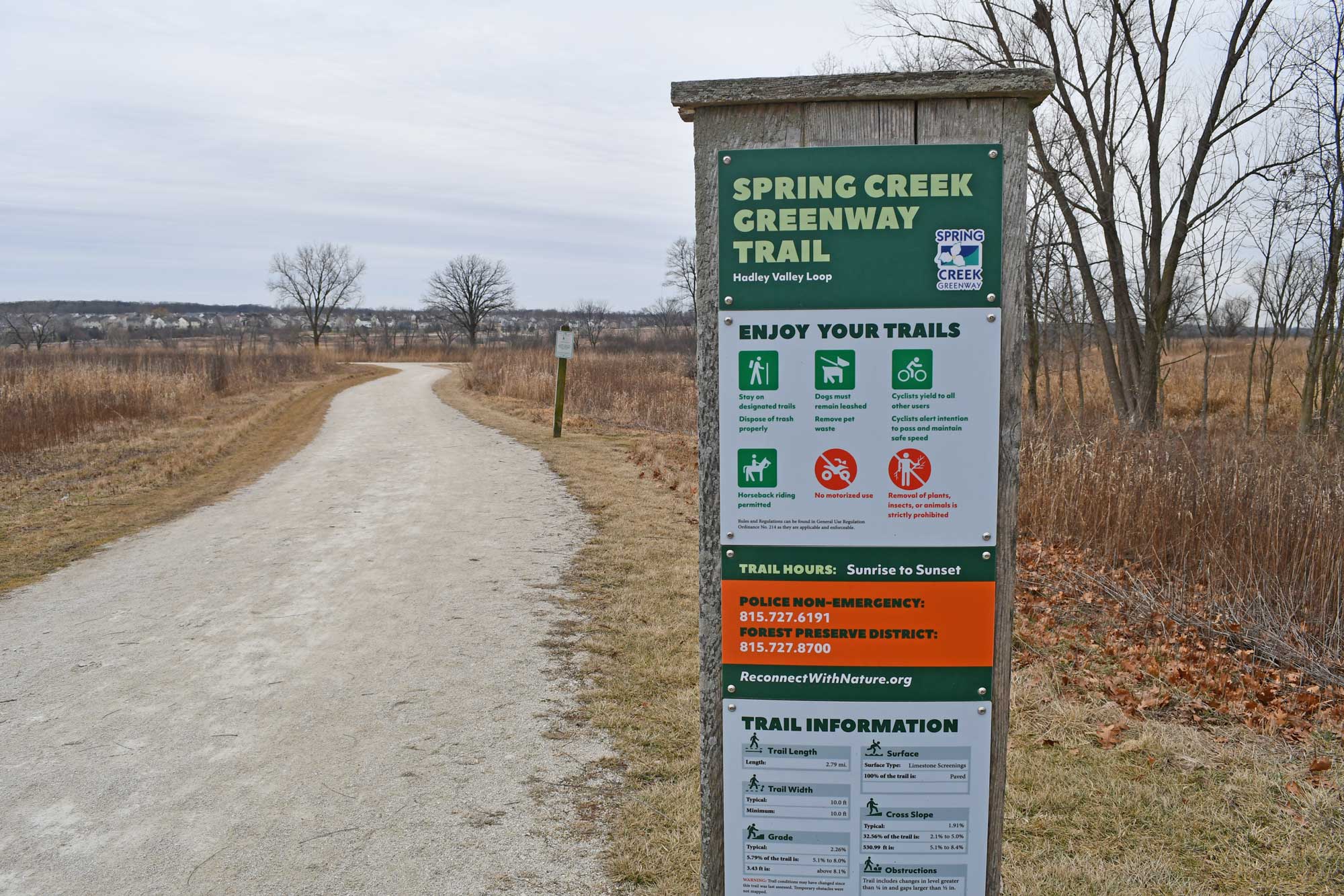 Trail sign with limestone trail, grasses, and vegetation in the background.