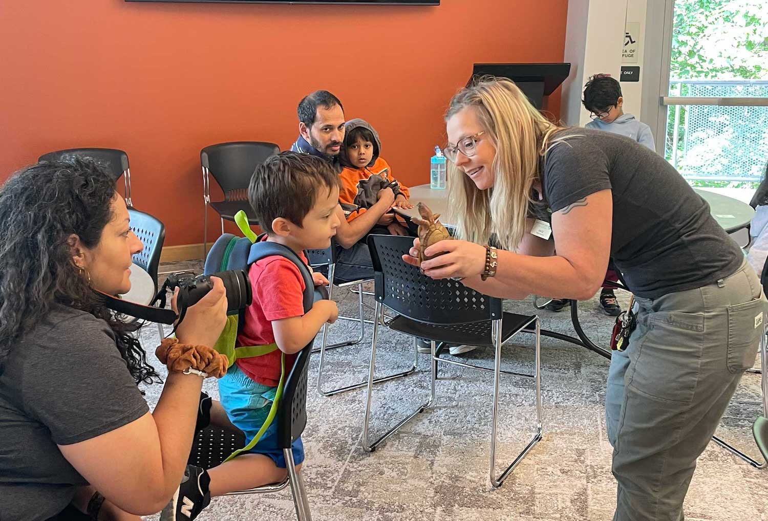 An adult holding a turtle up to a child with other people look on.