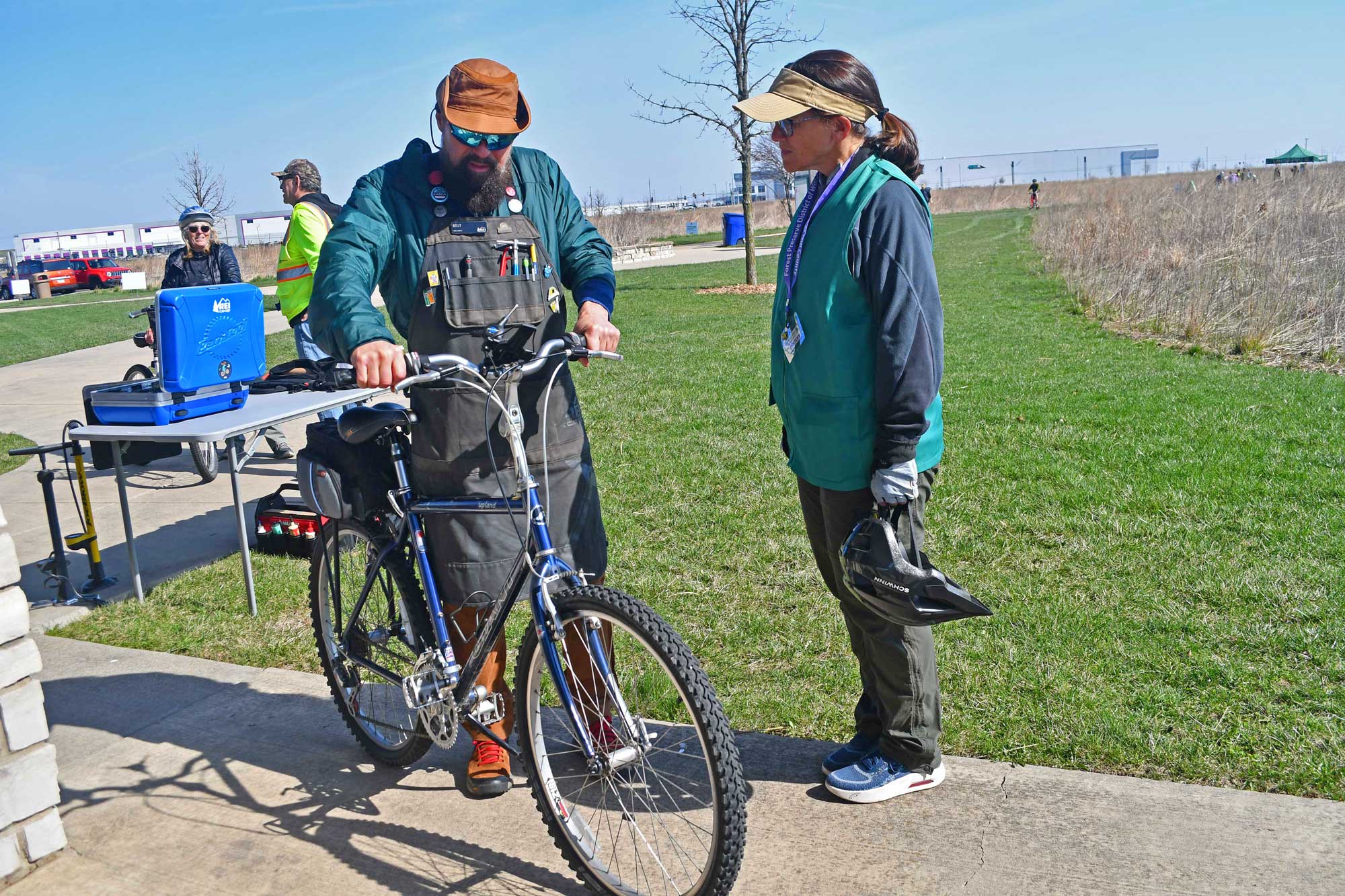 Person assisting another person with their bike near a trail.