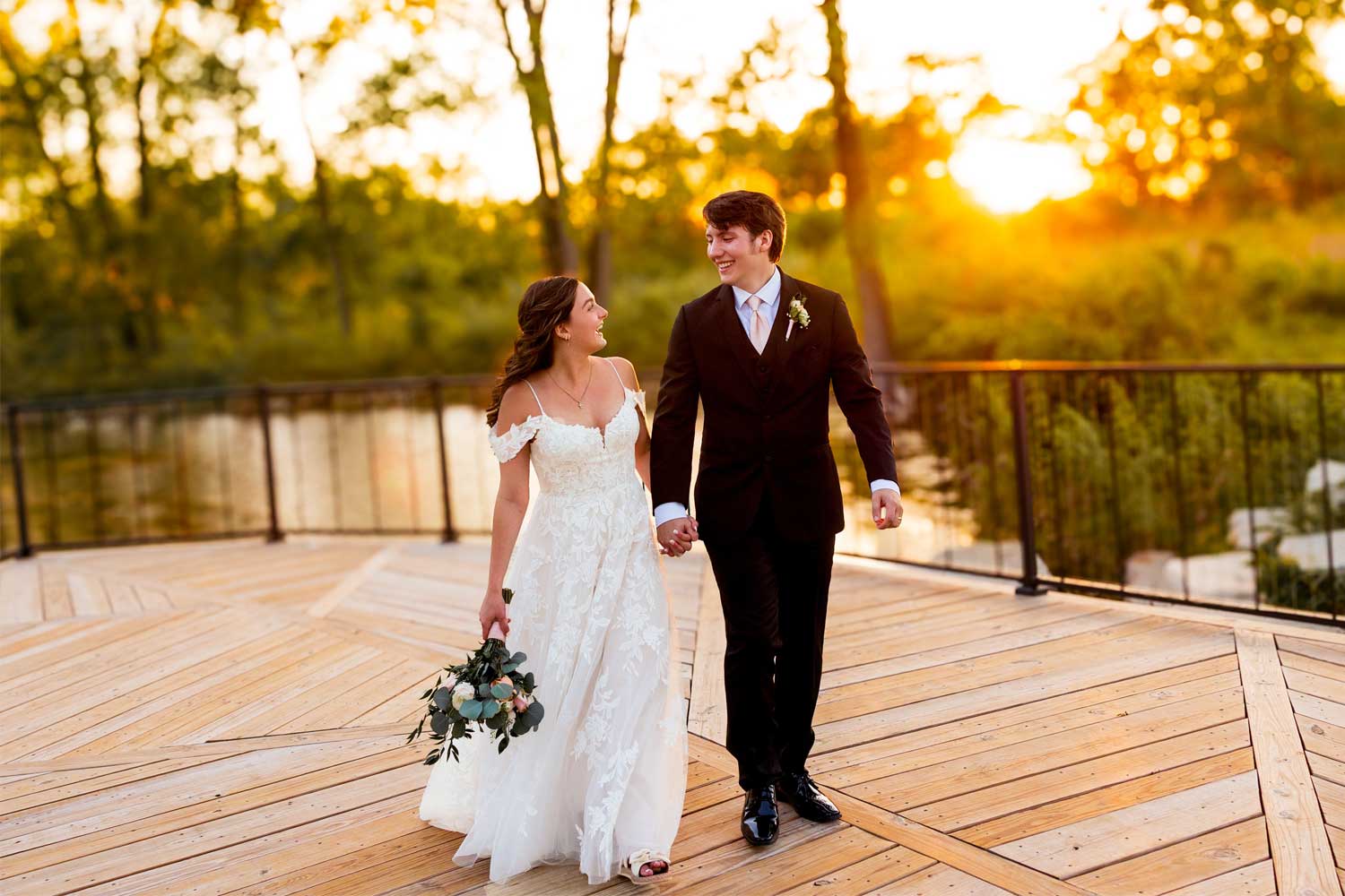 Newly married couple standing on a deck with the setting sun in the background.
