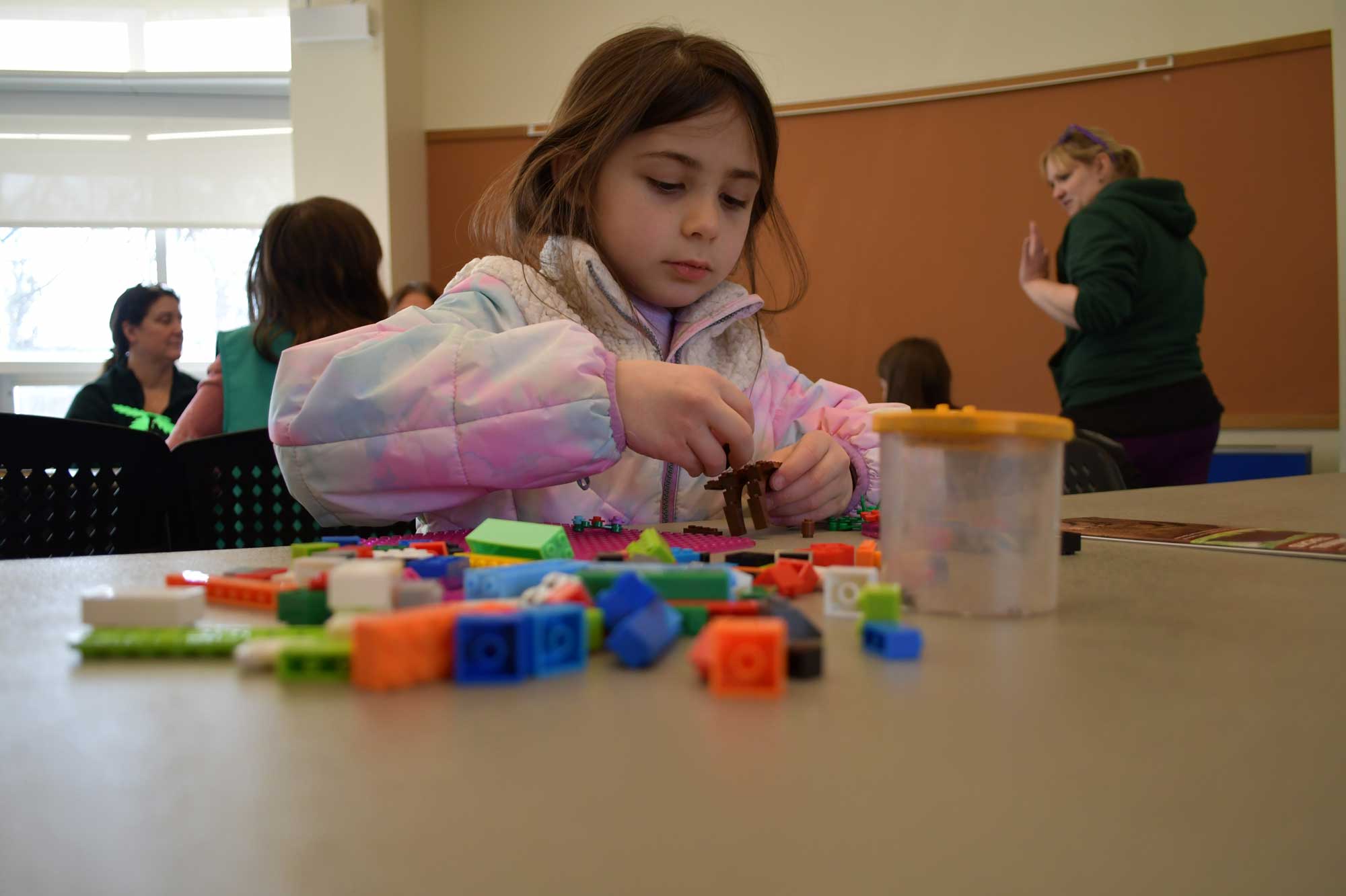 A child sitting at a table building something out of LEGOs.