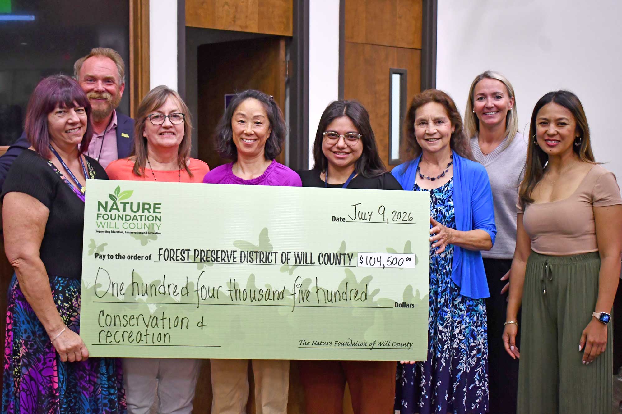 People stand in an office setting while holding a large donation check.