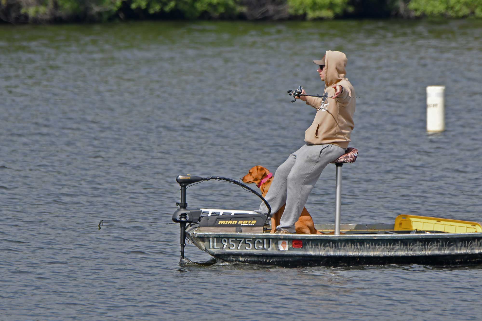 Person sitting in a boat while fishing with trees in the background.