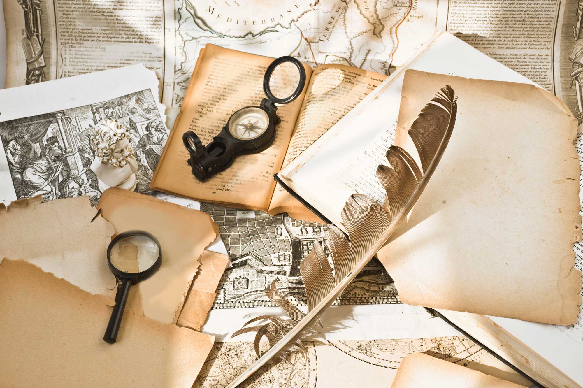 A collection of old envelopes, letters and photos along with a feather and magnifying glass on a table. 