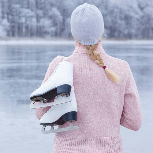 A person holding ice skates near a frozen lake.