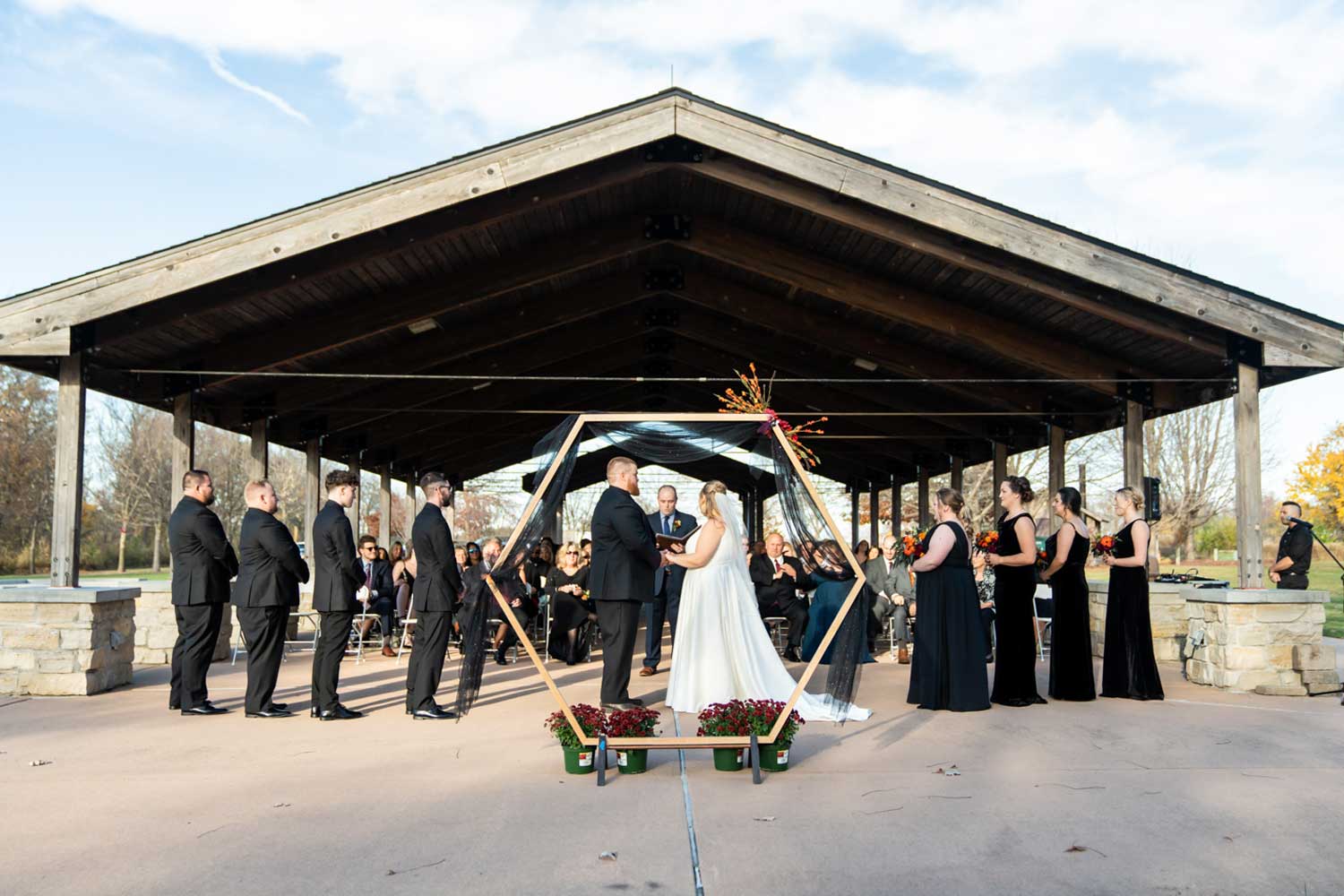 Wedding party standing at ceremony under outdoor shelter.
