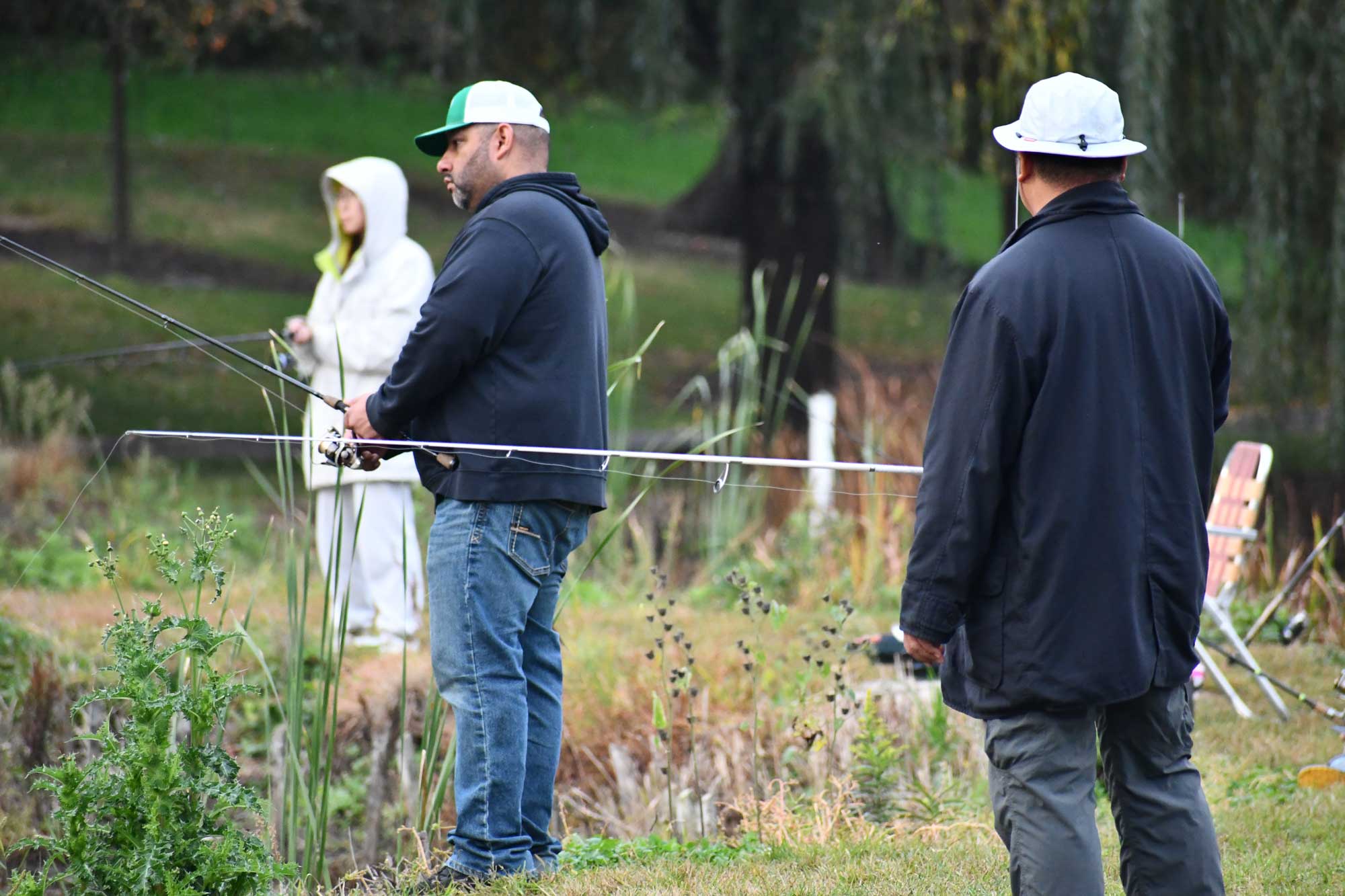 Three people holding fishing poles while standing along a shore. 