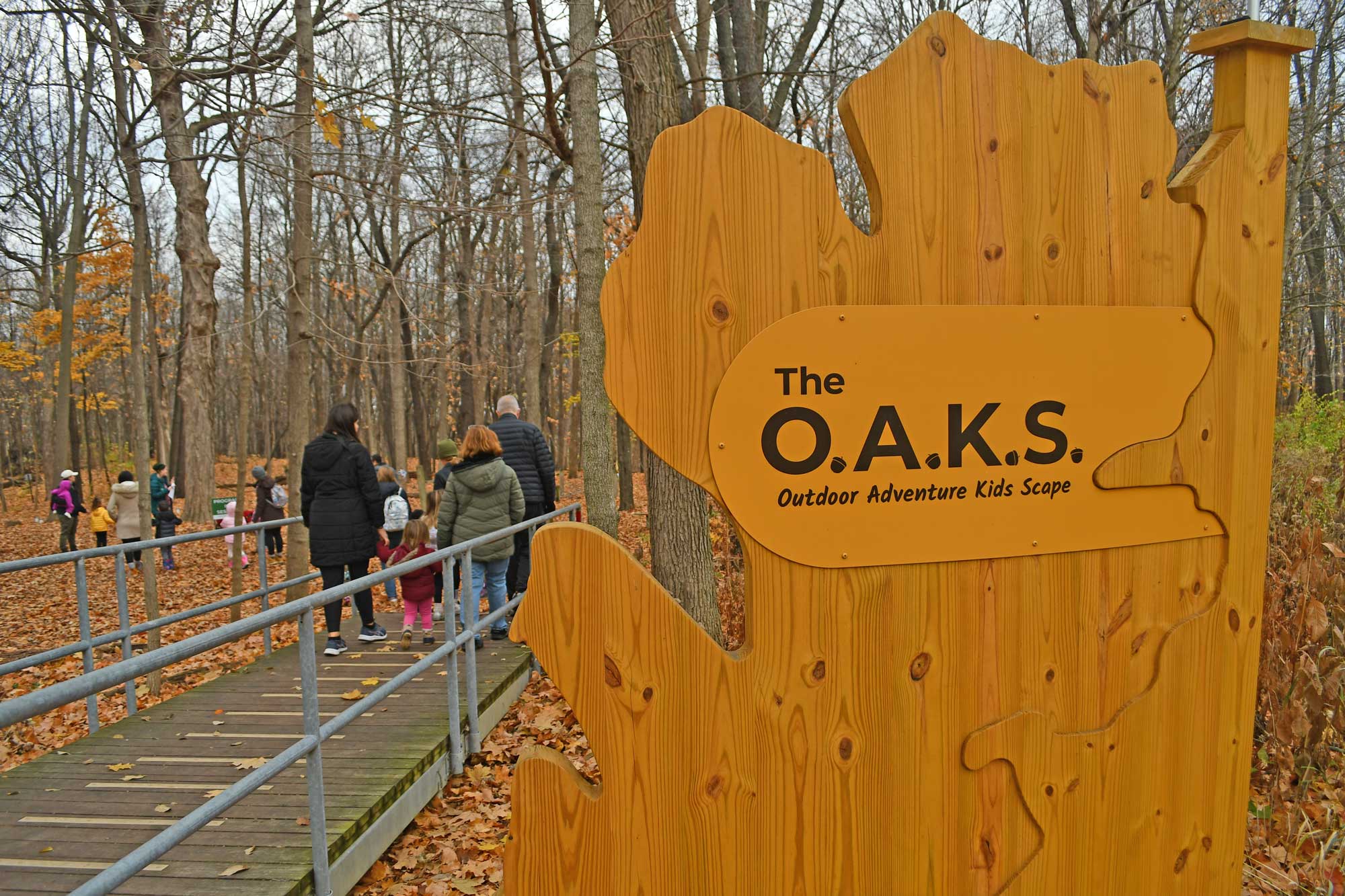 Sign for kids play area with people and trees in the background.