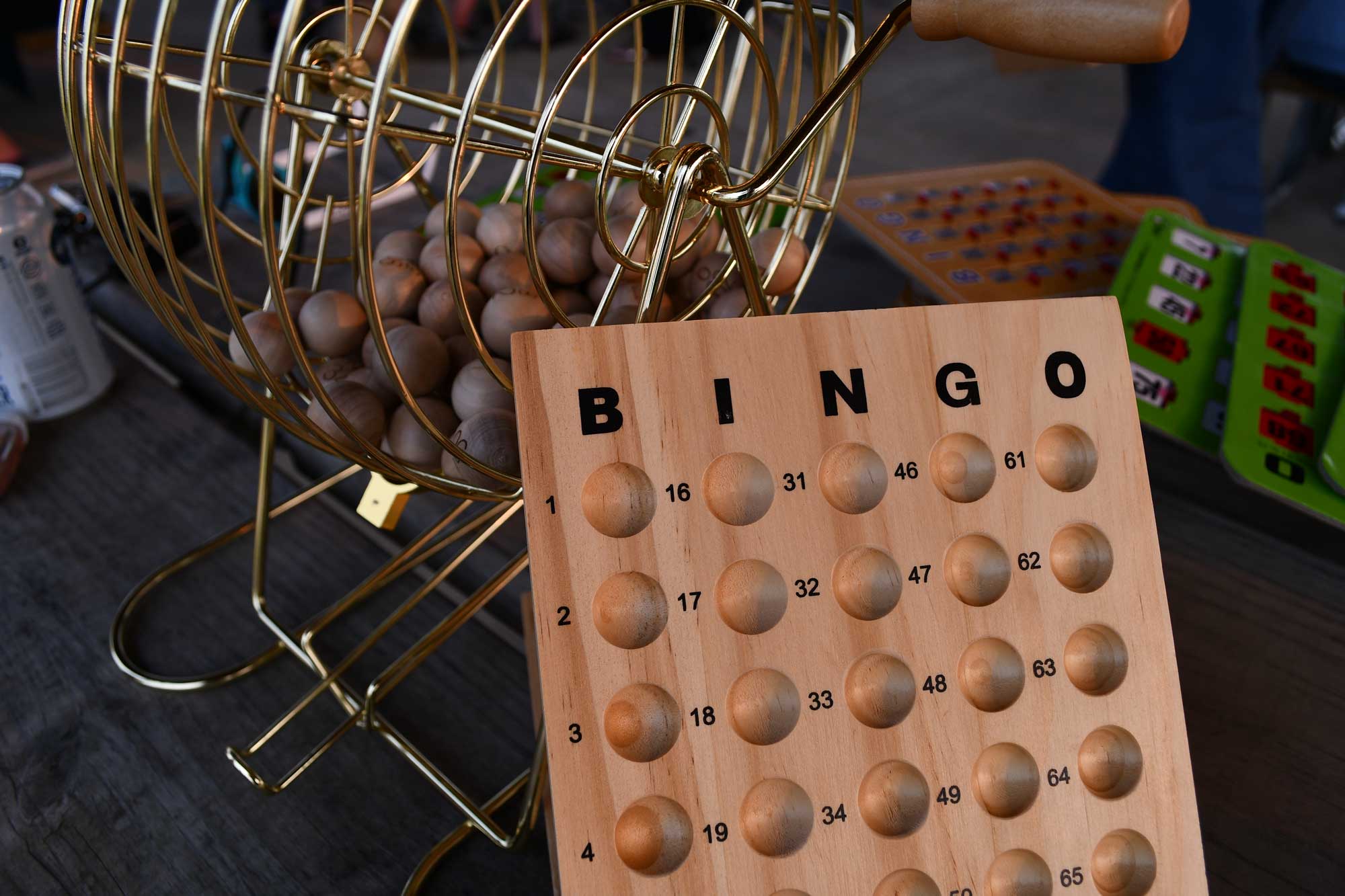 A bingo ball spinner and a bingo number holder on a wooden picnic table.