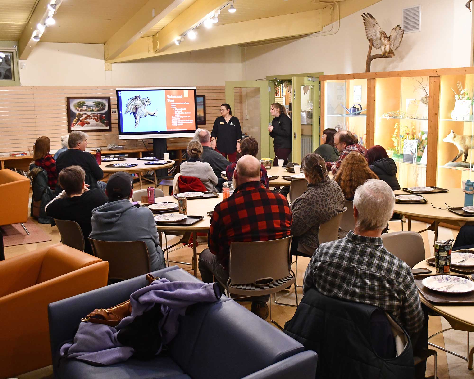 a group of people sitting at tables and a woman giving a presentation