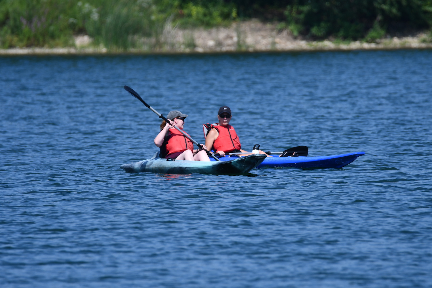 Two people in blue kayaks on a lake. One person is holding their paddle up in the air.