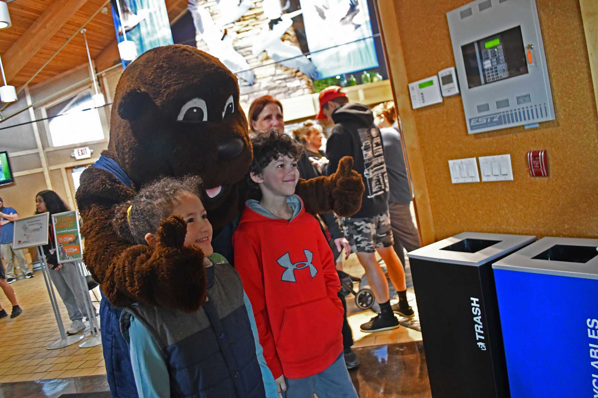 Person in a mascot costume posing with two kids at a program in a nature center.