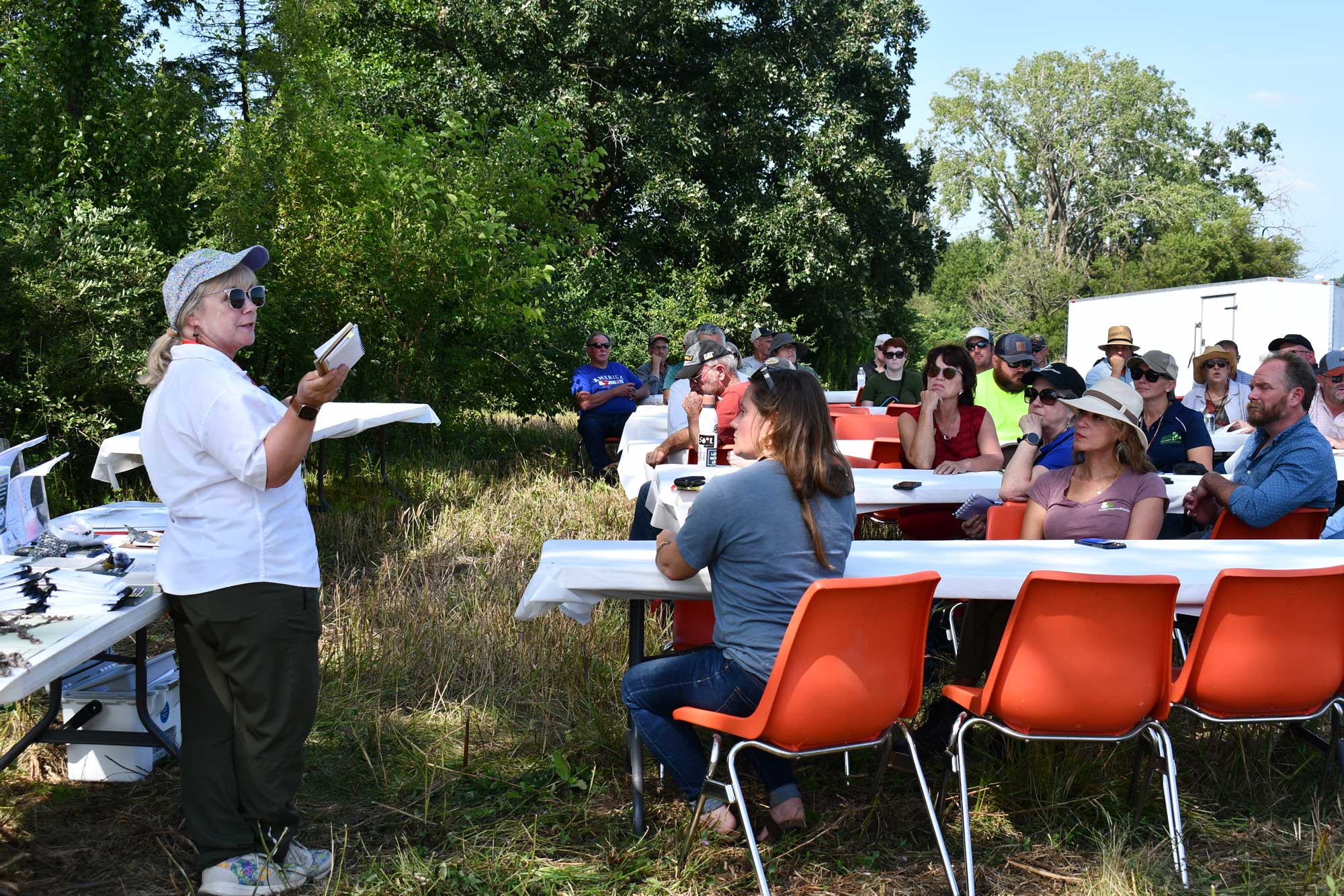People sit around tables in a farm field. 