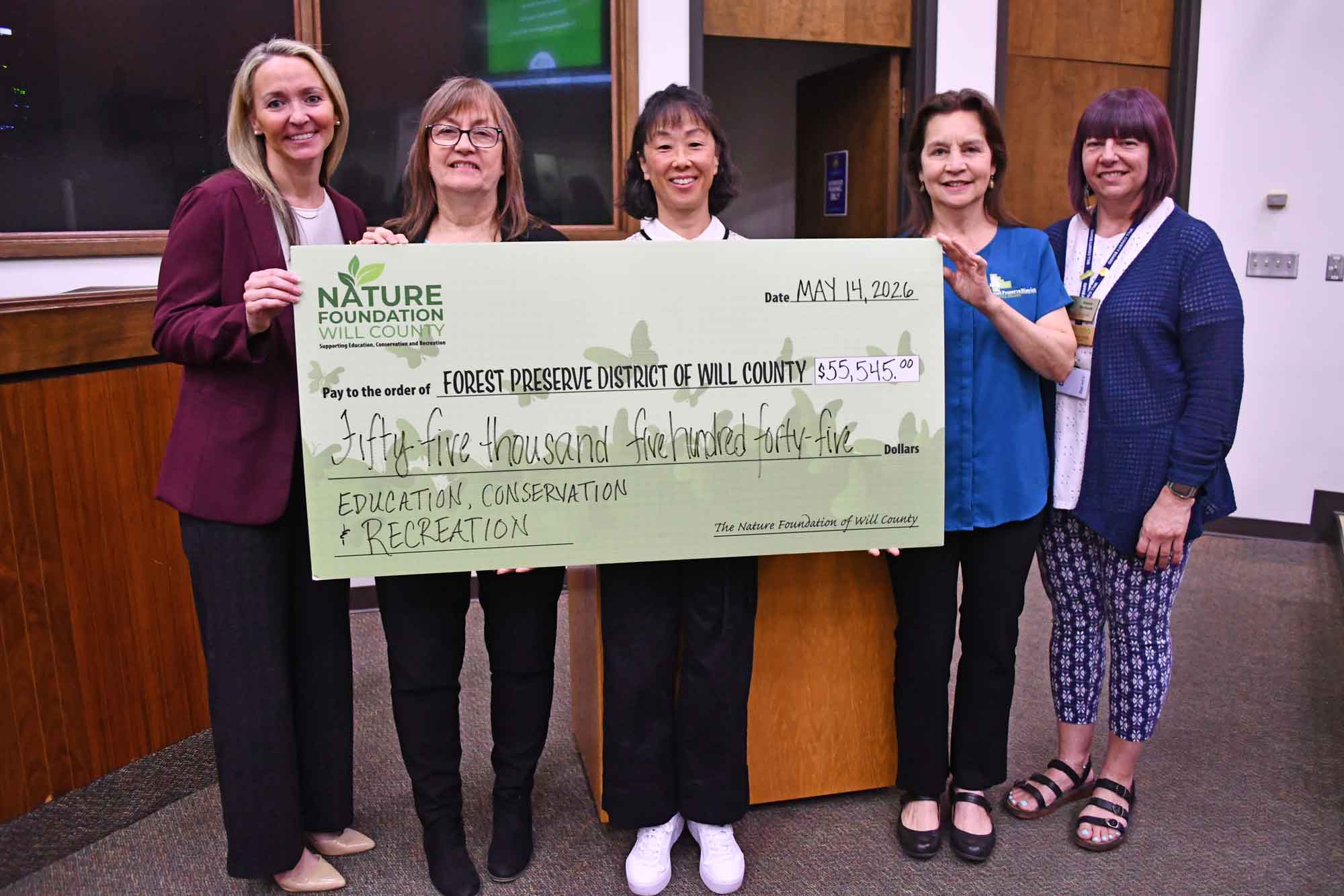 People stand in a room while holding a large donation check. 