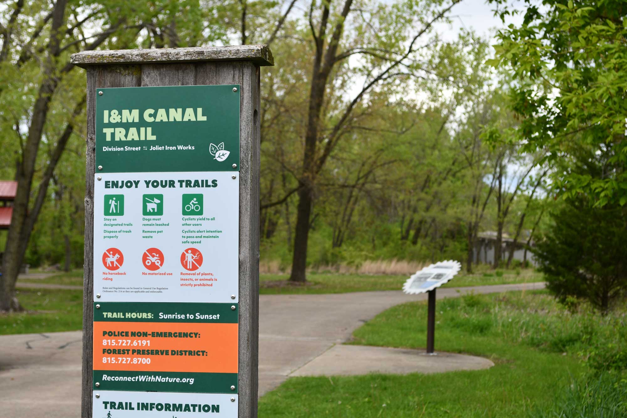 Trail sign with paved trail and trees in the background.