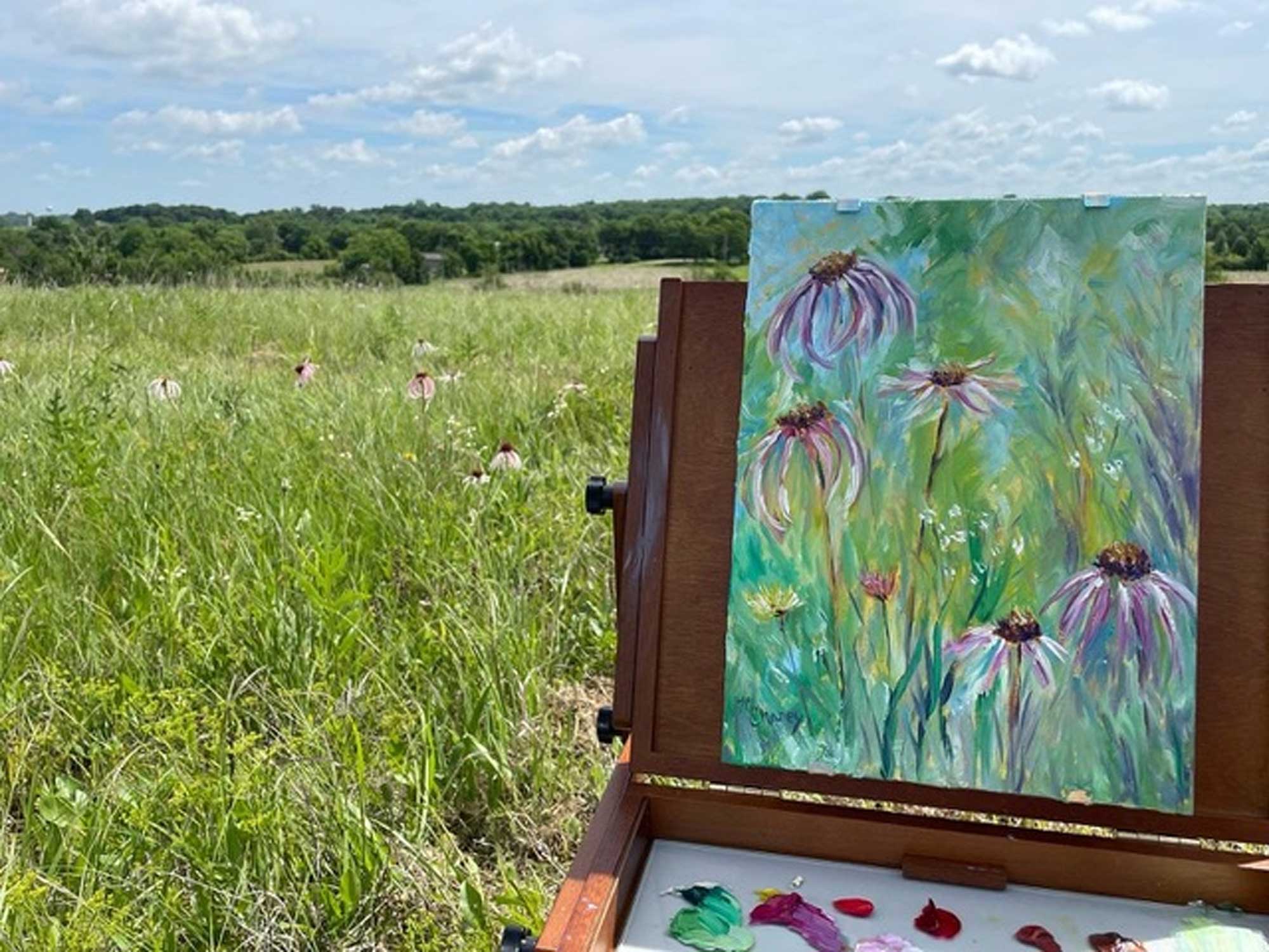 An easel with a painting of wildflowers set up in a prairie.