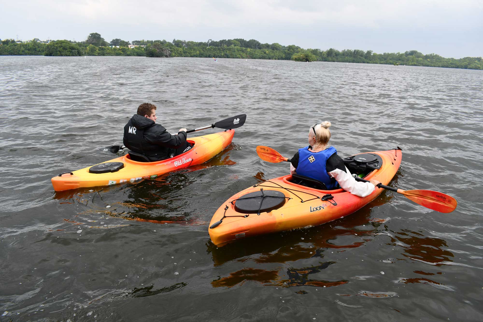 Two people kayaking with water and trees in the background.