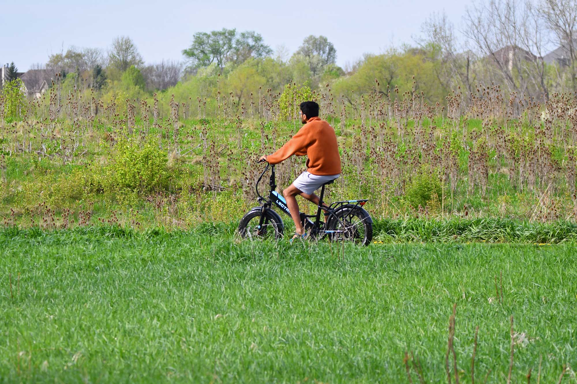 Person riding a bike with grass, vegetation, and trees in the background.