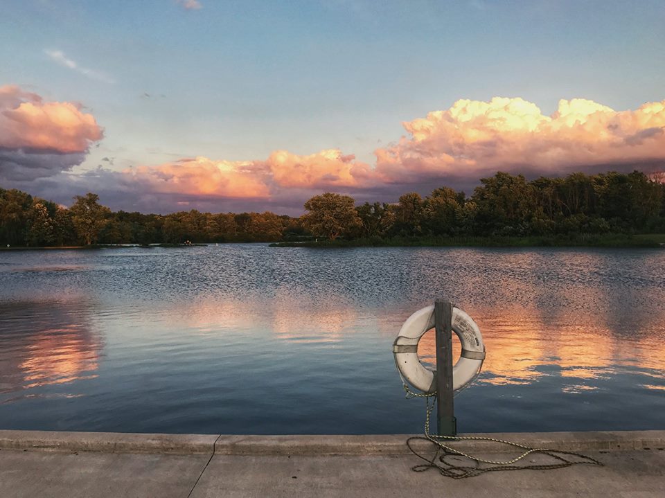 A calm lake at sunset, with pink and purple hues in the clouds in the sky and reflected in the water below.
