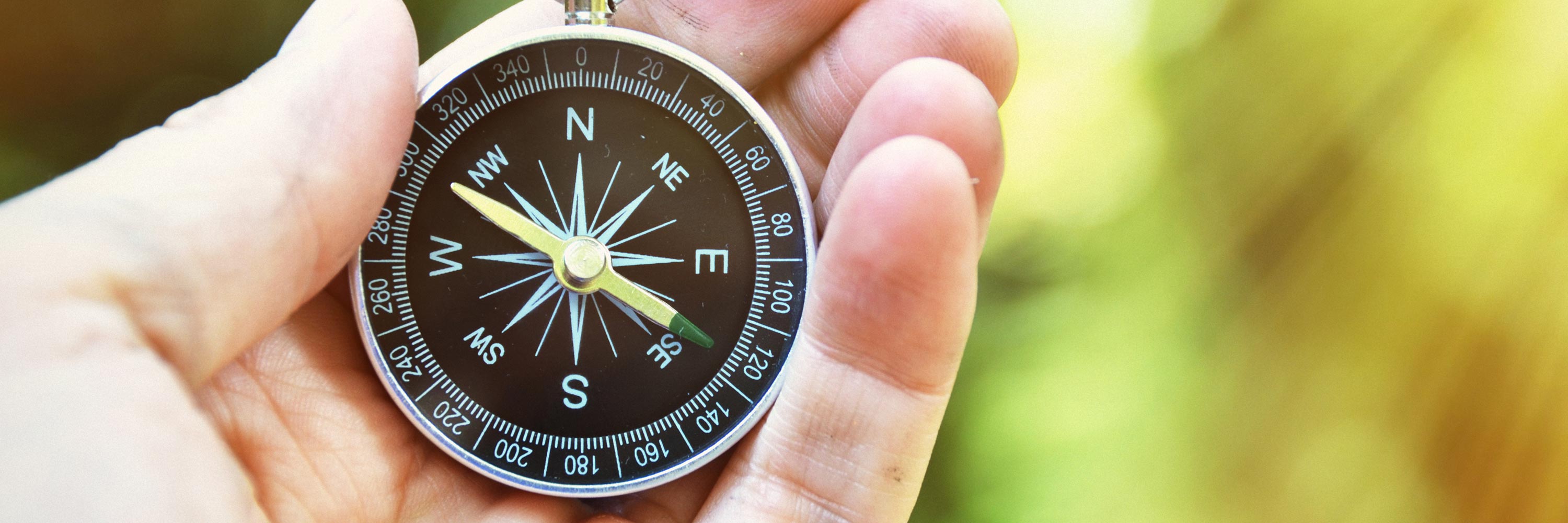 A closeup of a black compass with a yellow directional arrow pointing to the upper left being help in a person's hand.