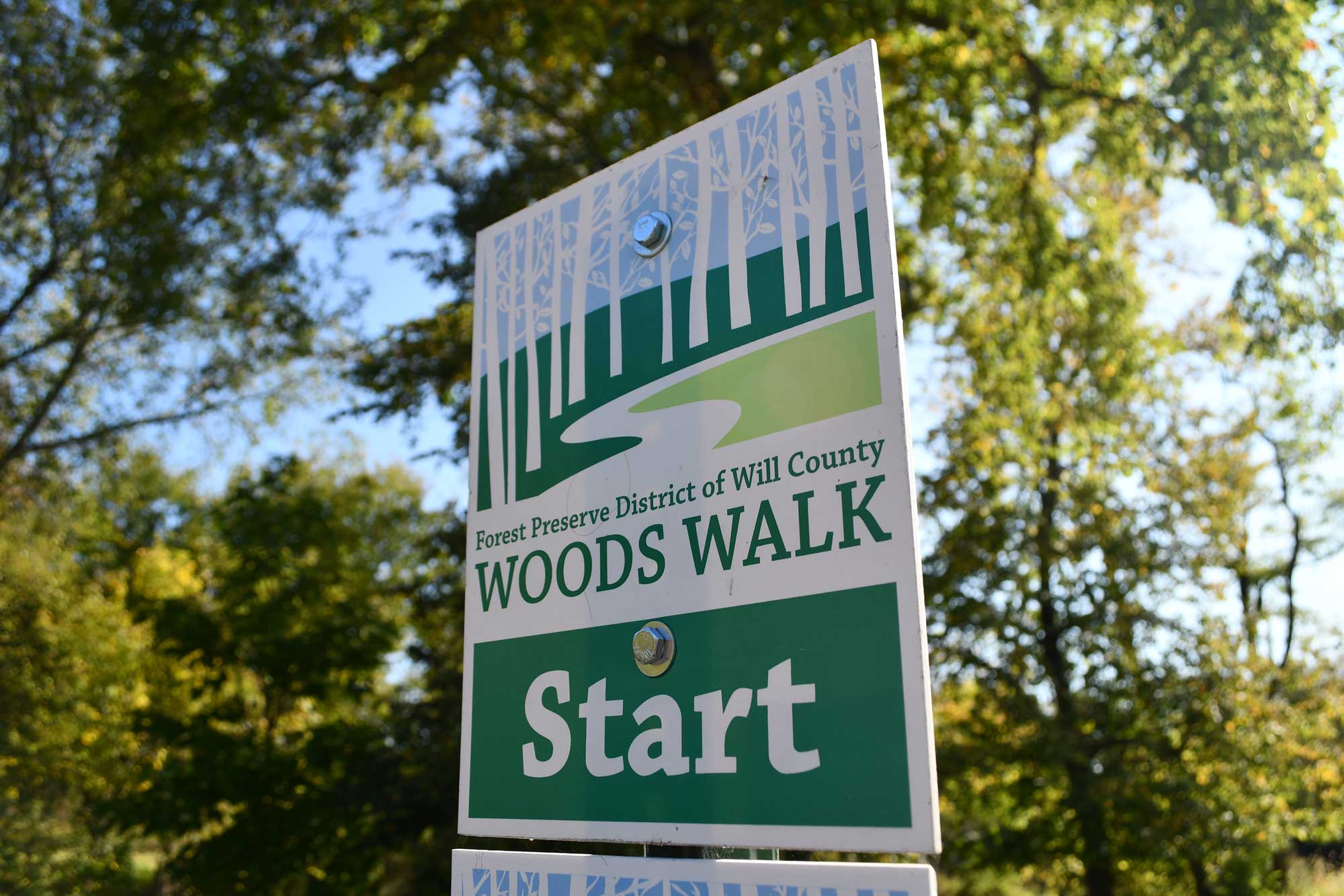 A green and white Woods Walk sign along a trail.