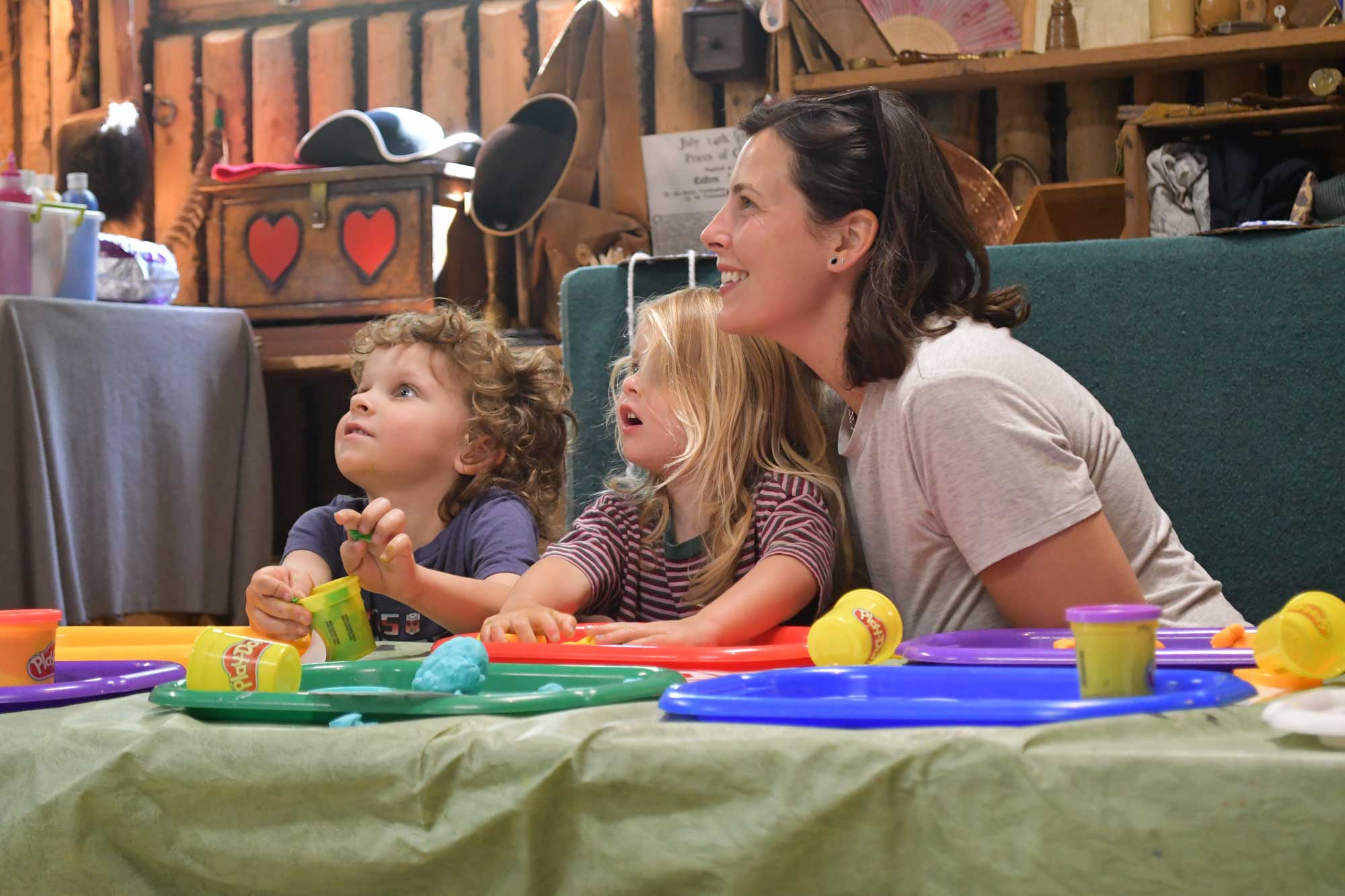 An adults and two kids looking up from a table with colorful plates.