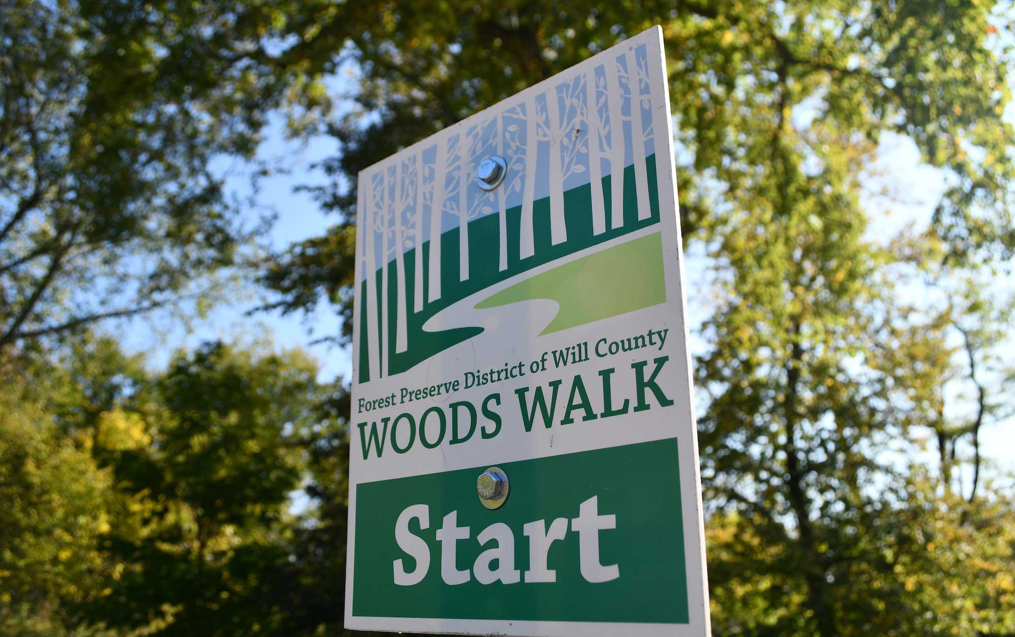 A sign for Woods Walk with trees in the background.