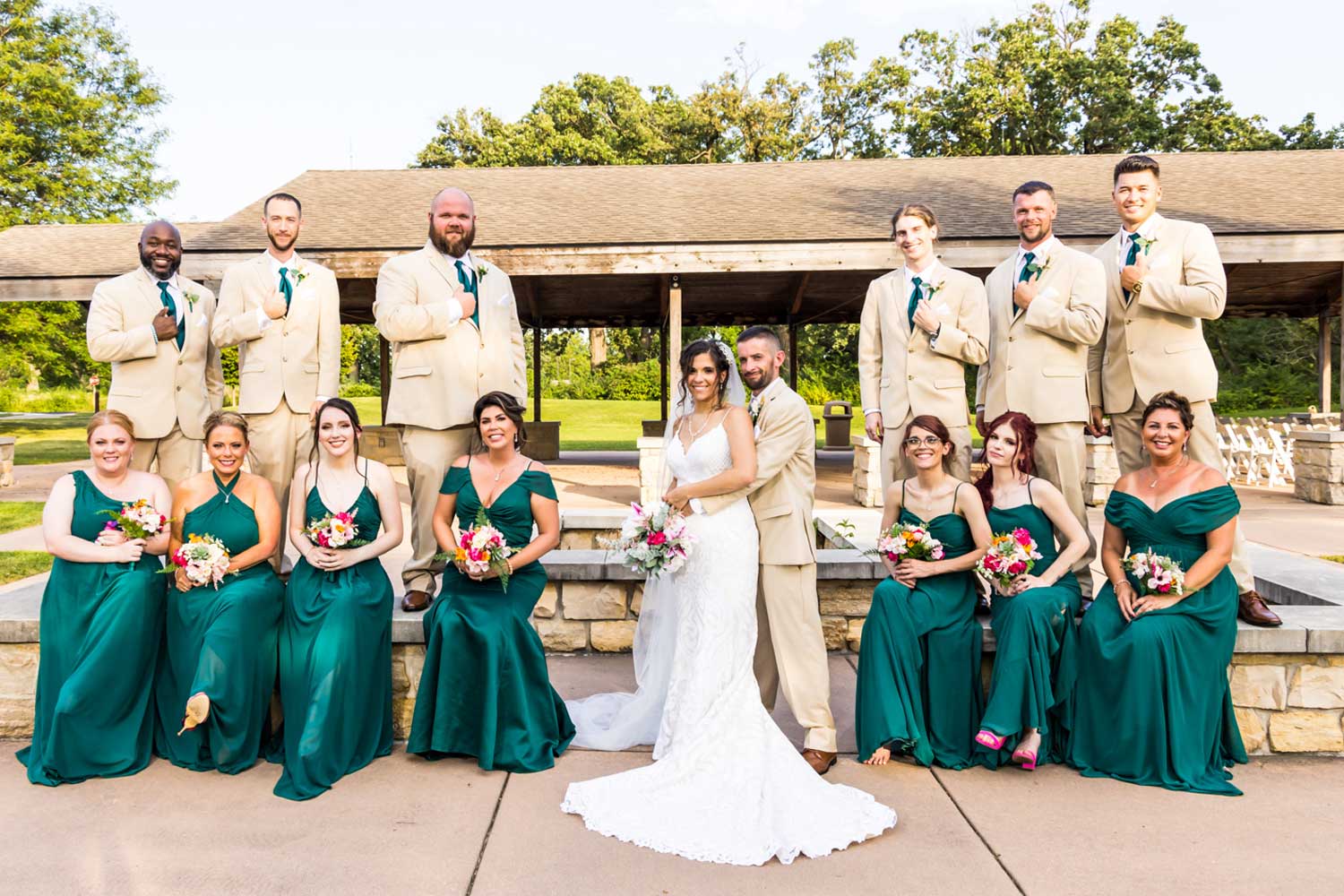 Wedding party standing in front of outdoor shelter.