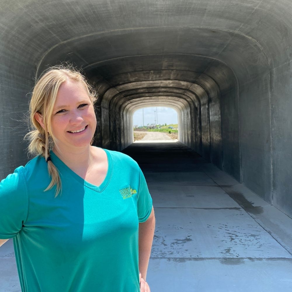 A Forest Preserve employee stands smiling at the entrance of a large concrete pedestrian tunnel on a sunny day.
