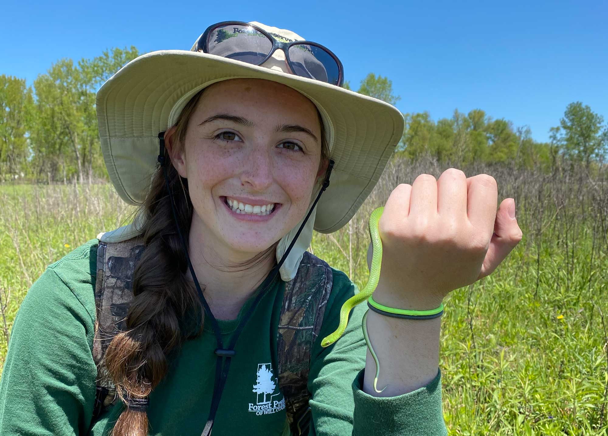 An ecologist poses with a greensnake on a sunny day.