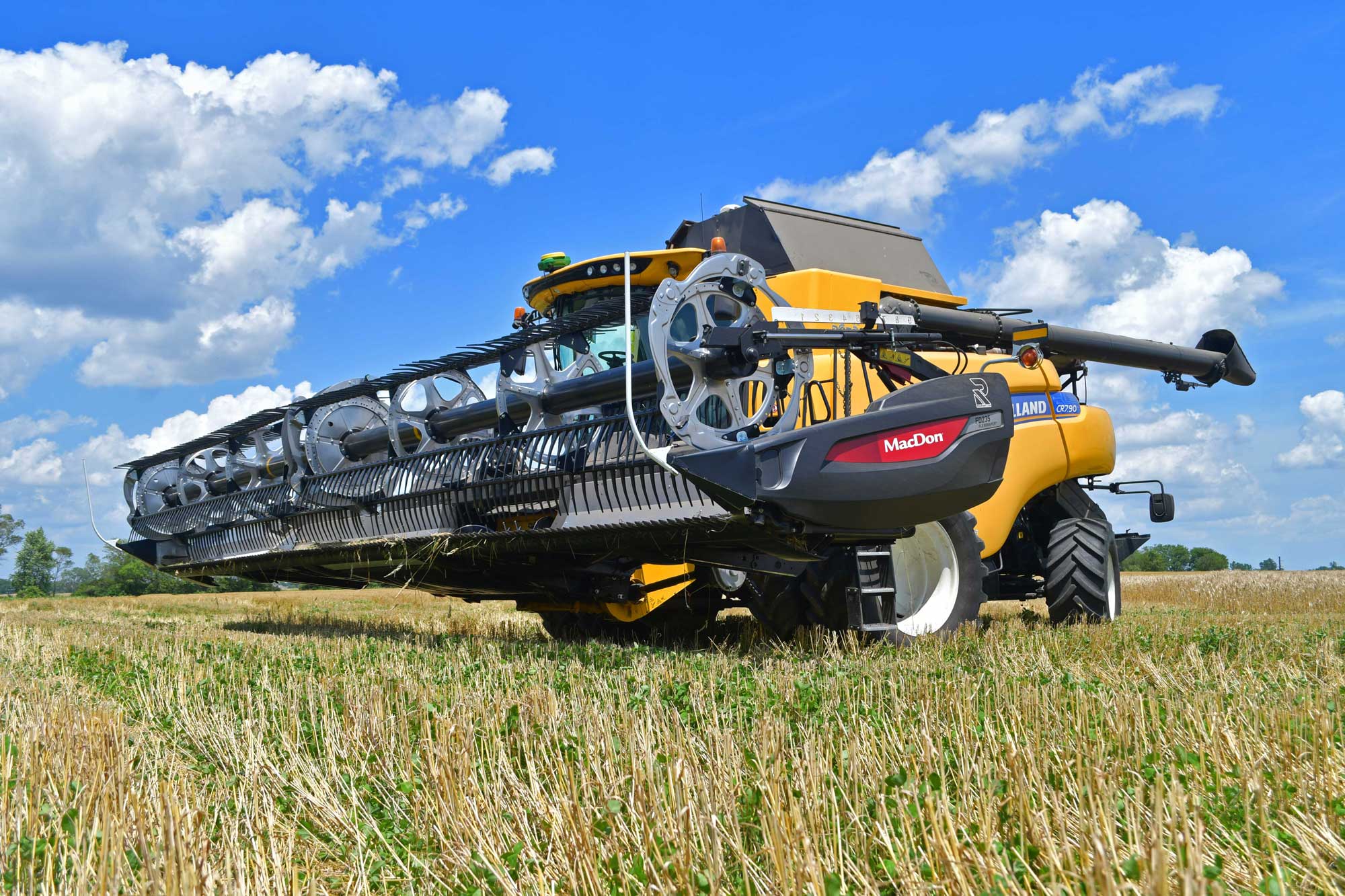 Combine sitting in a wheat farm field with a partly cloudy sky in the background.