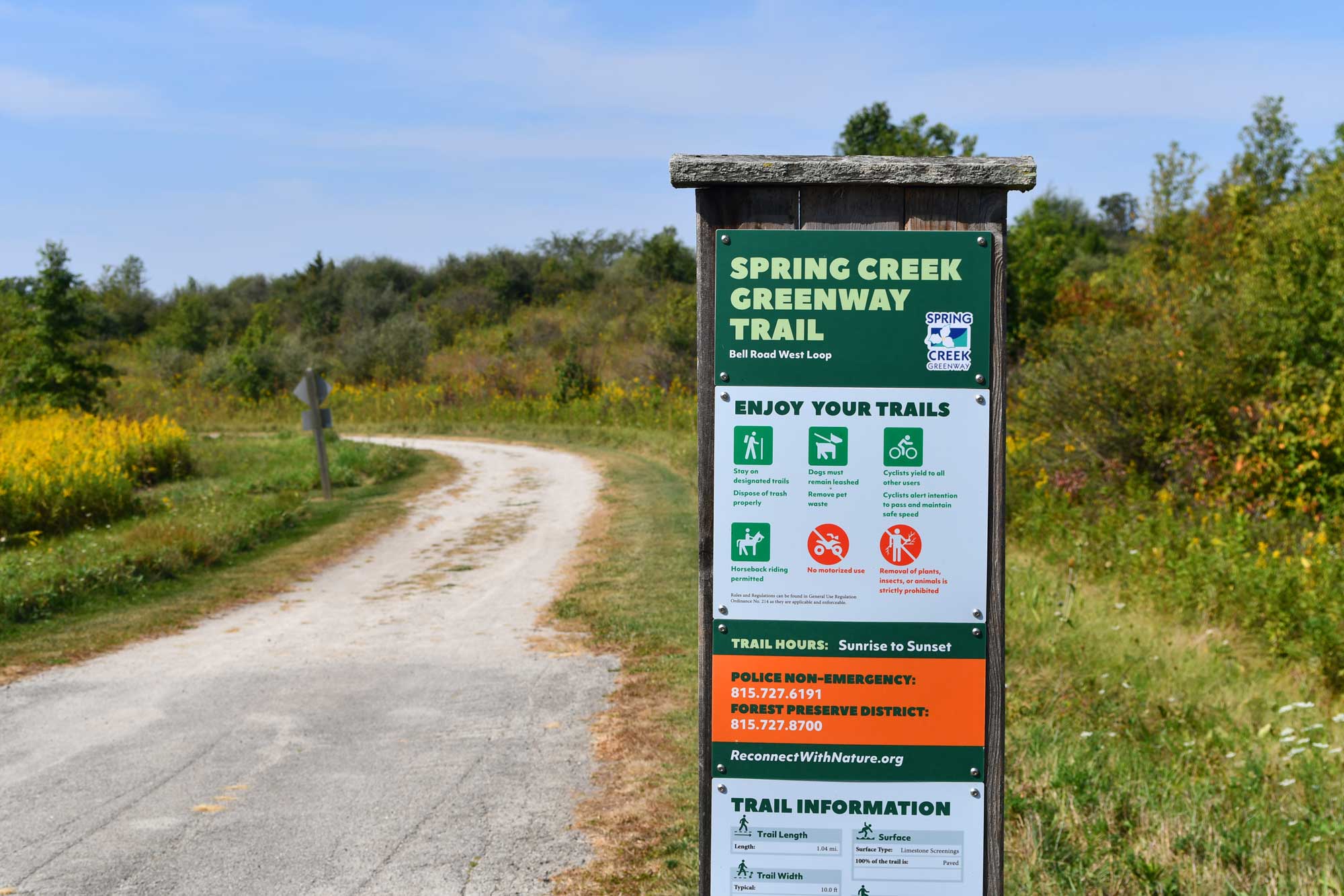 Trail sign with limestone trail, grasses, and vegetation in the background.