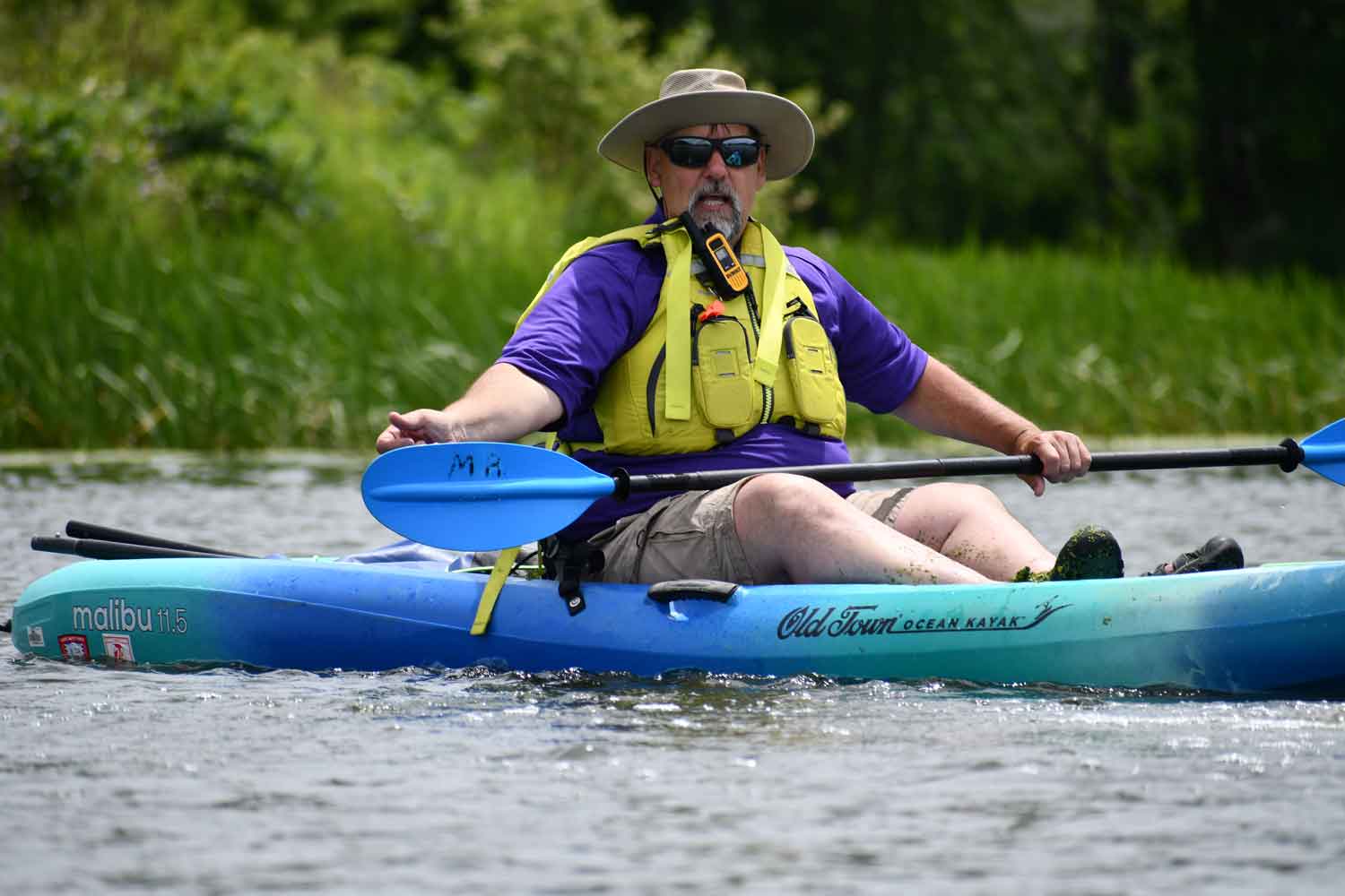 A person sitting in a kayak on the water holding their paddle up out of the water.