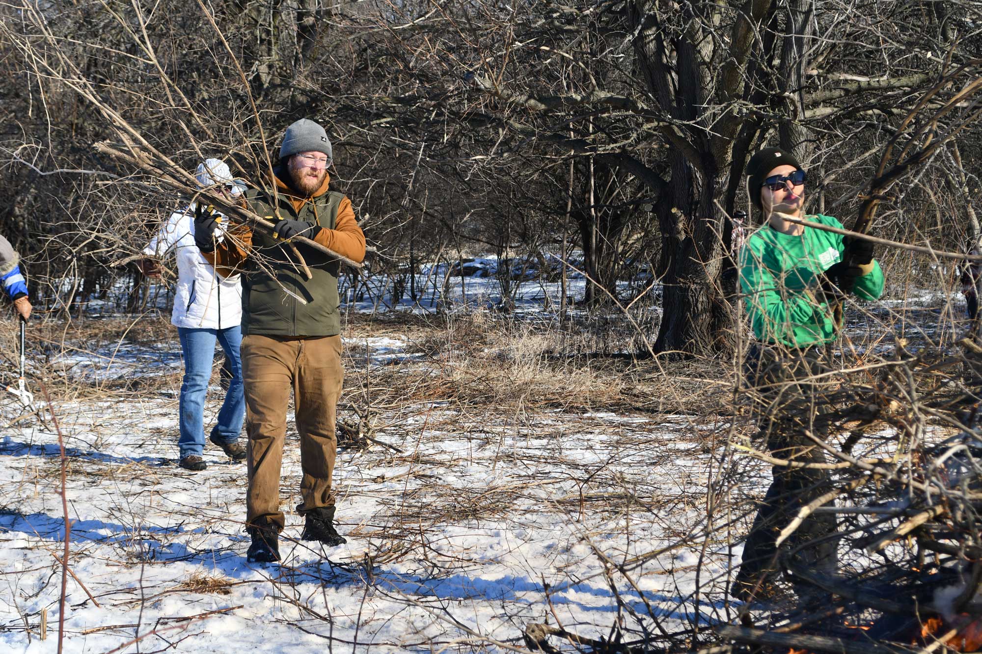 Two people adding branches to a brush pile. Light snow is on the ground.