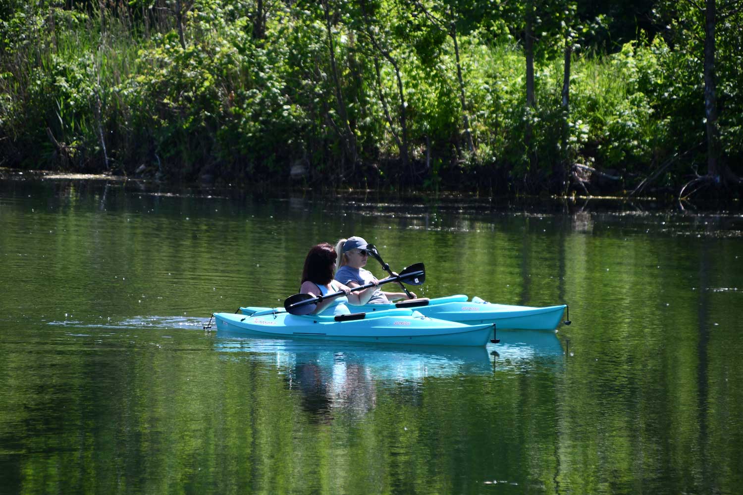 Two people in kayaks on still water.