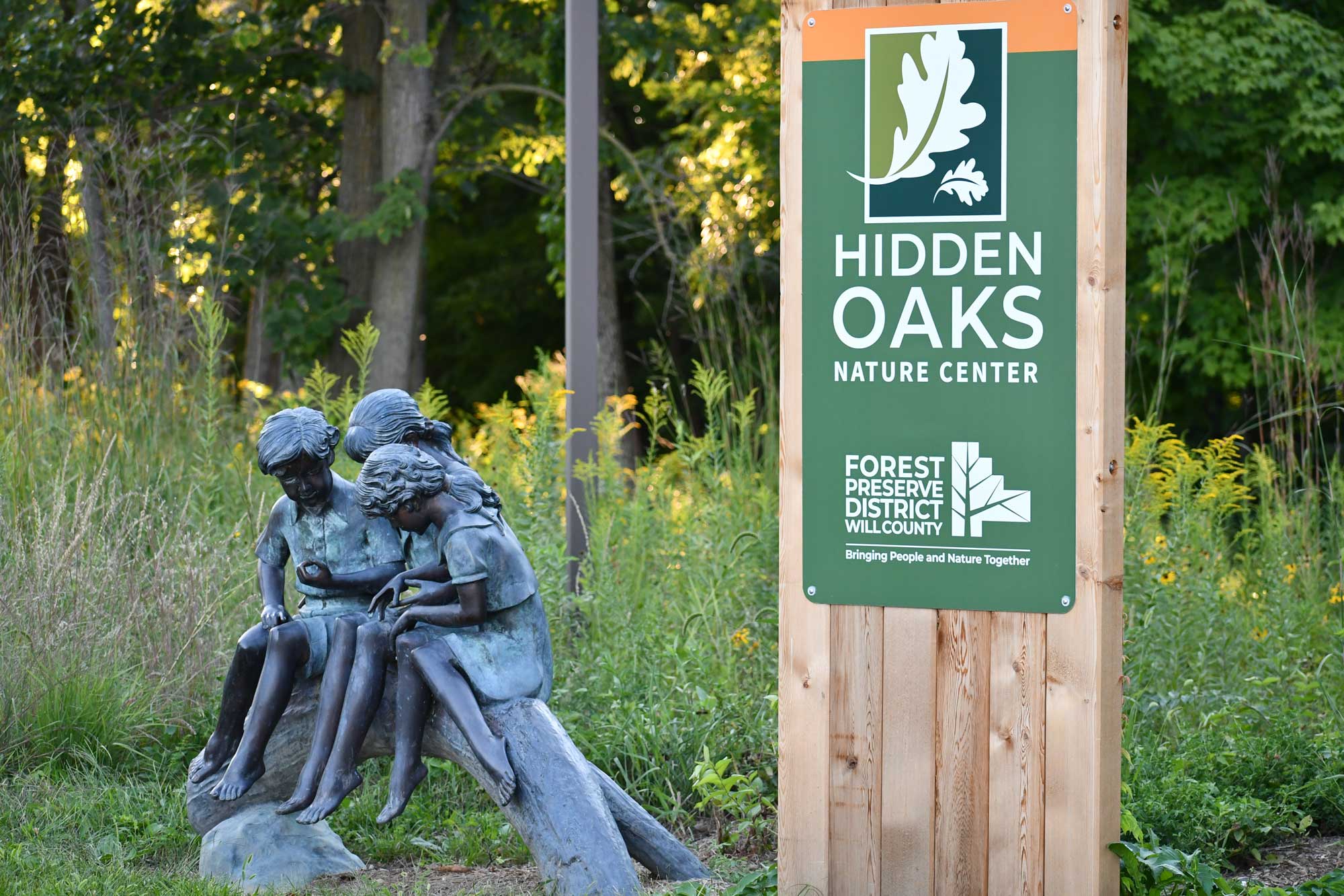 Hidden Oaks sign and a structure of three children on a log.