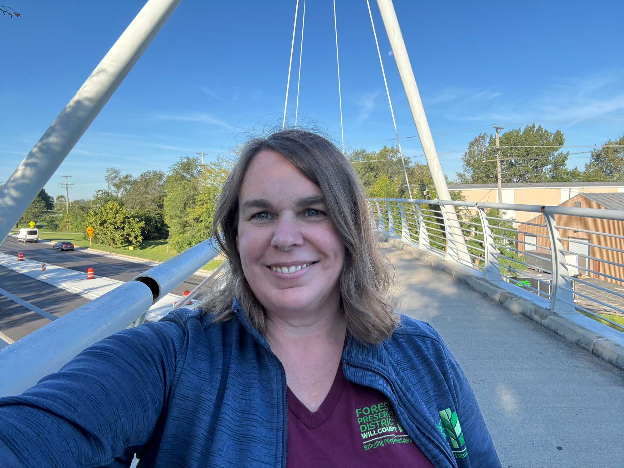 A person in a selfie taken on a white suspension bridge over a road. 
