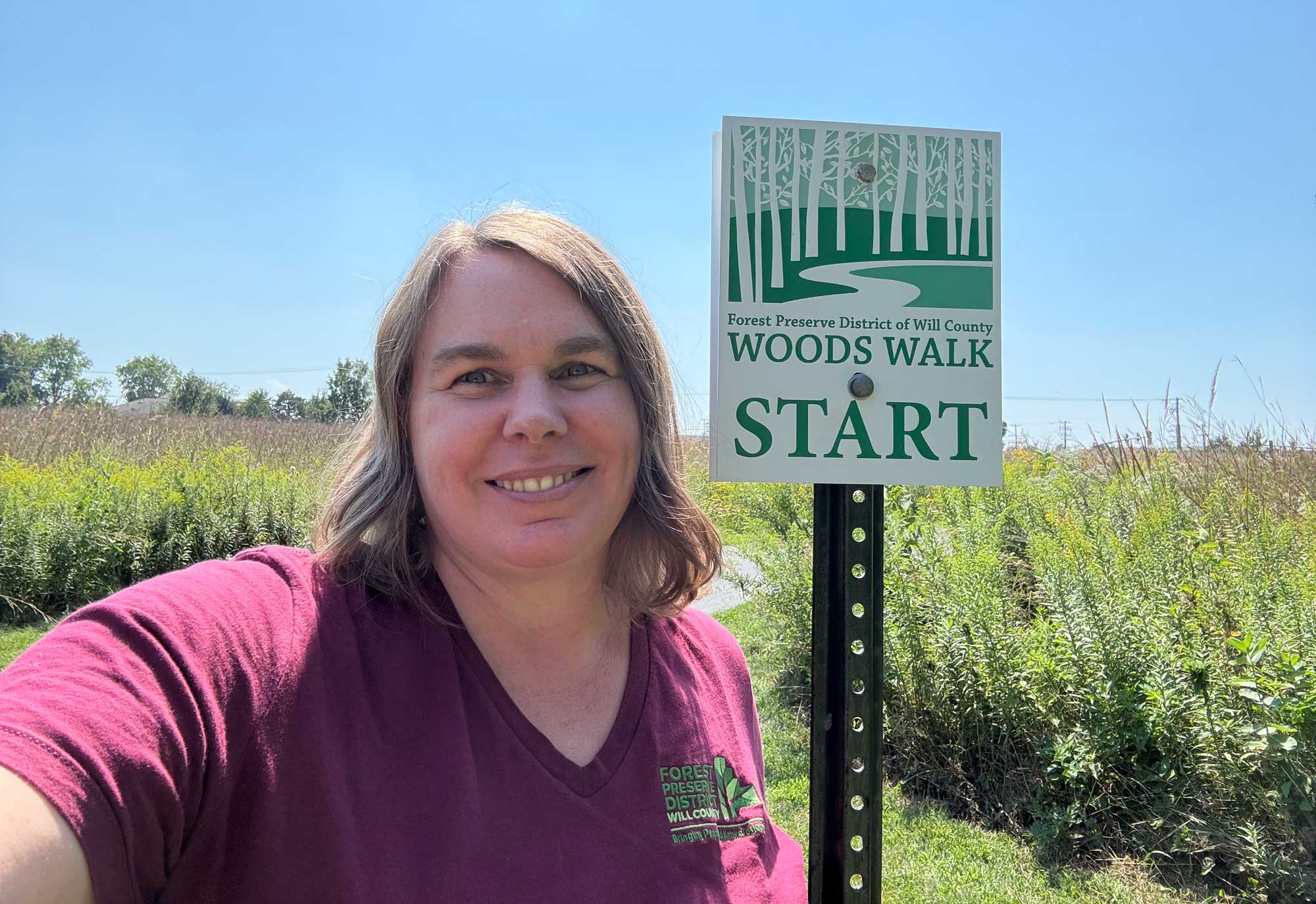 A person poses for a selfie next to a sign that says Woods Walk.