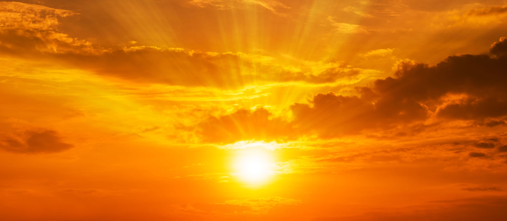 The setting sun shining bright in an orange sky.