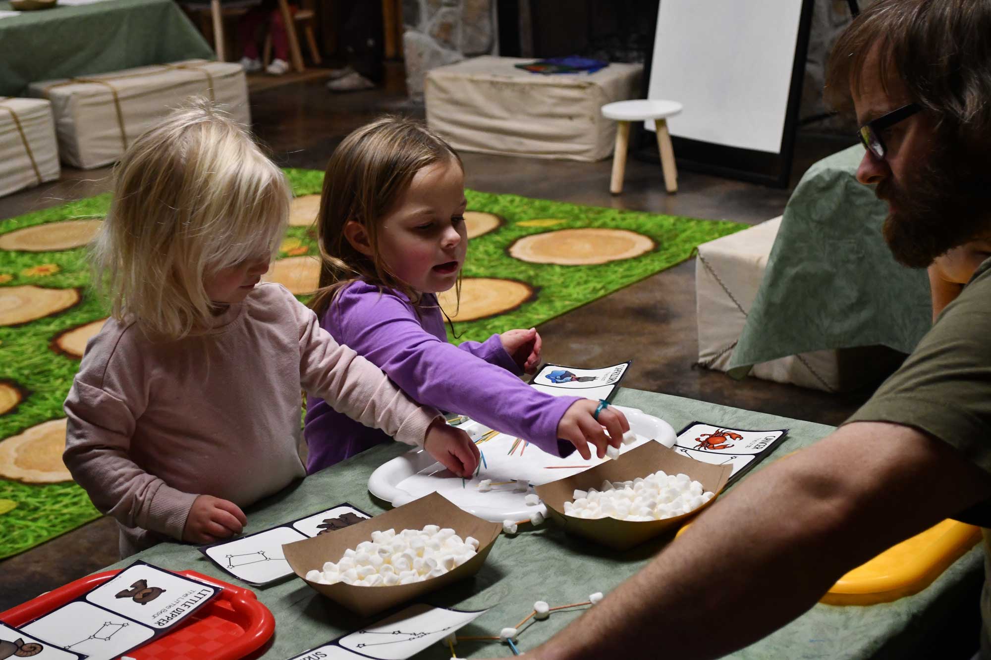 Two children sitting at a table working on an activity with an adult sitting across from them.
