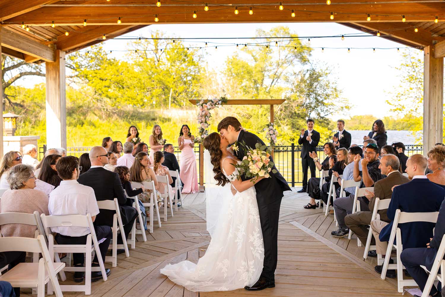 Couple sharing a kiss in the aisle surrounded by their guests.