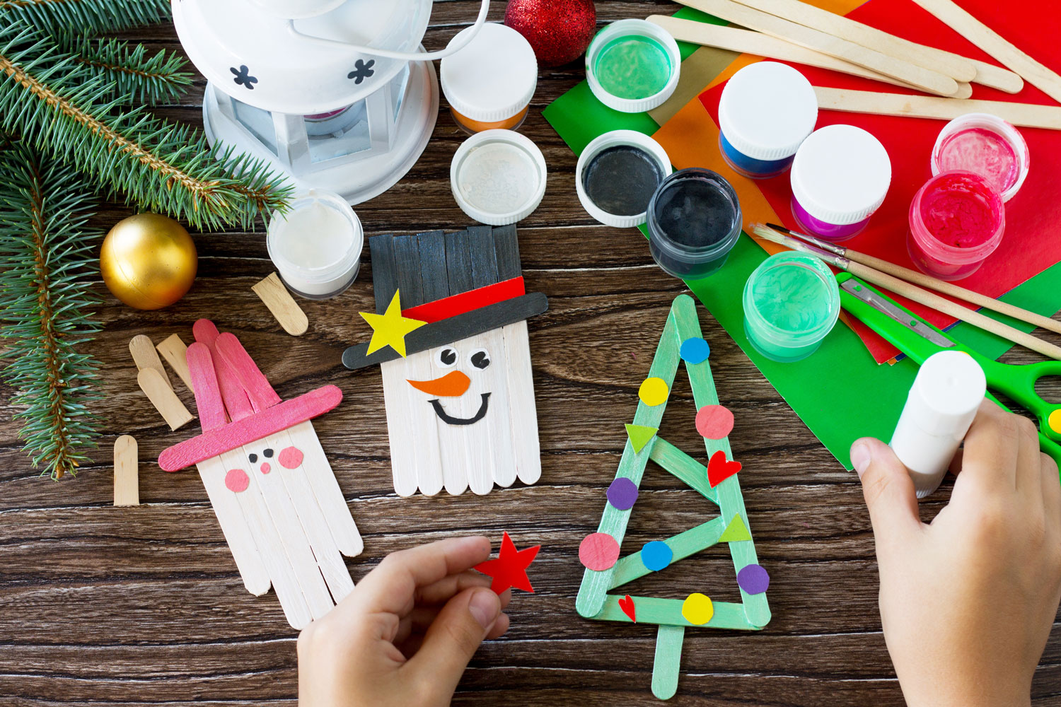 Winter crafts made of Popsicle sticks on a table with paints and other craft supplies. 