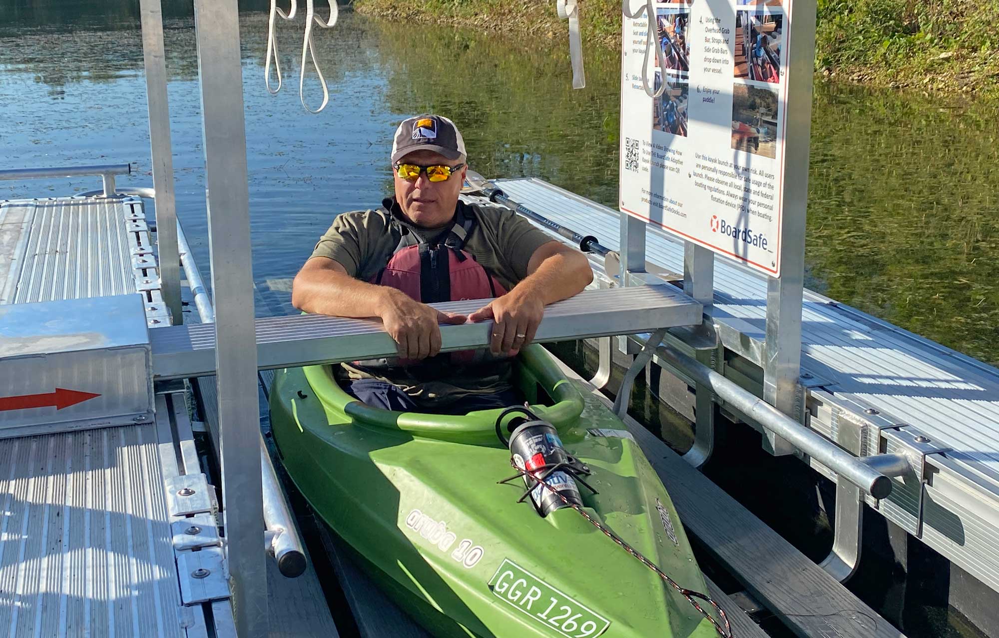A person using an accessible kayak launch with water in the background.