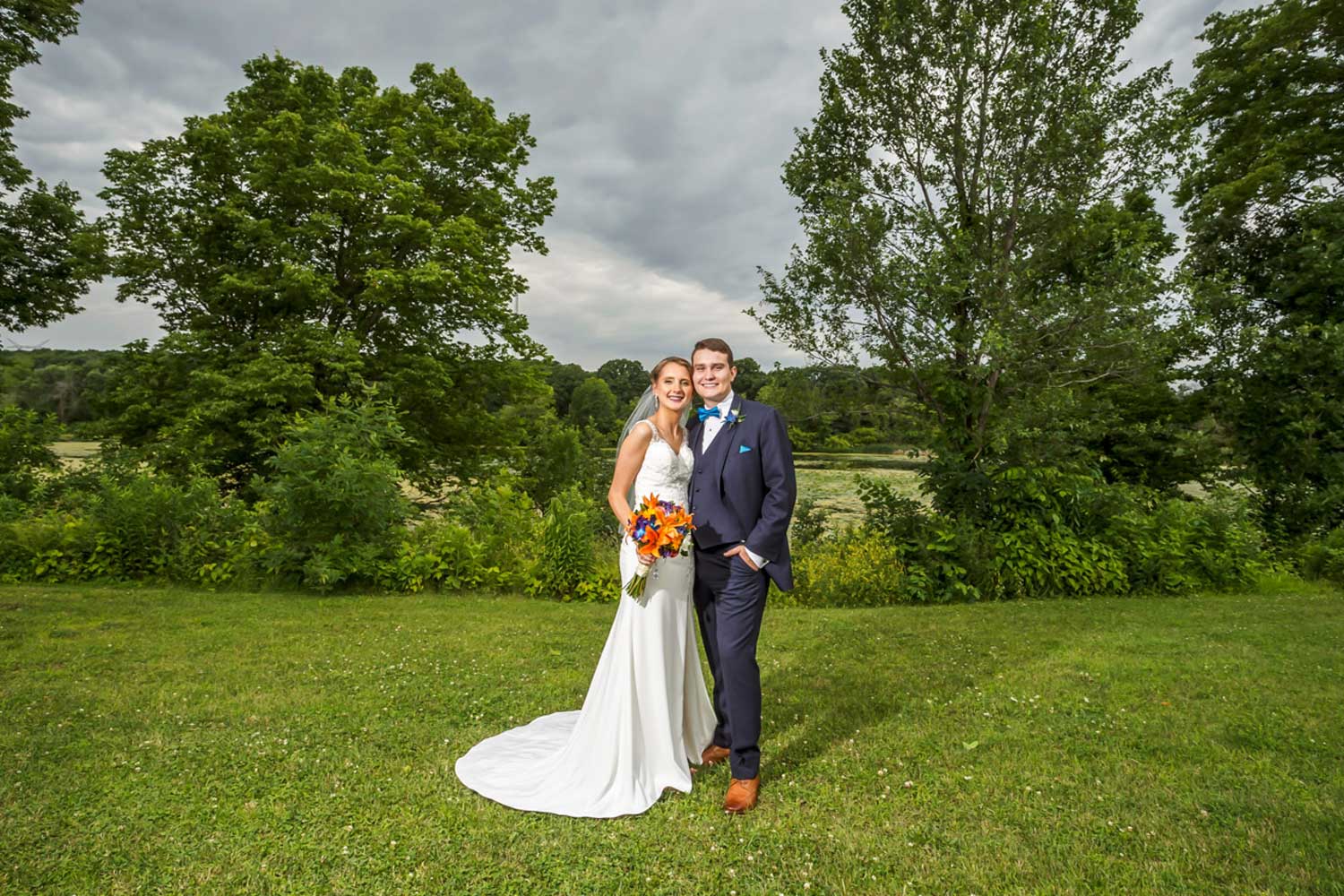 Newly married couple posing in front of the tree line.