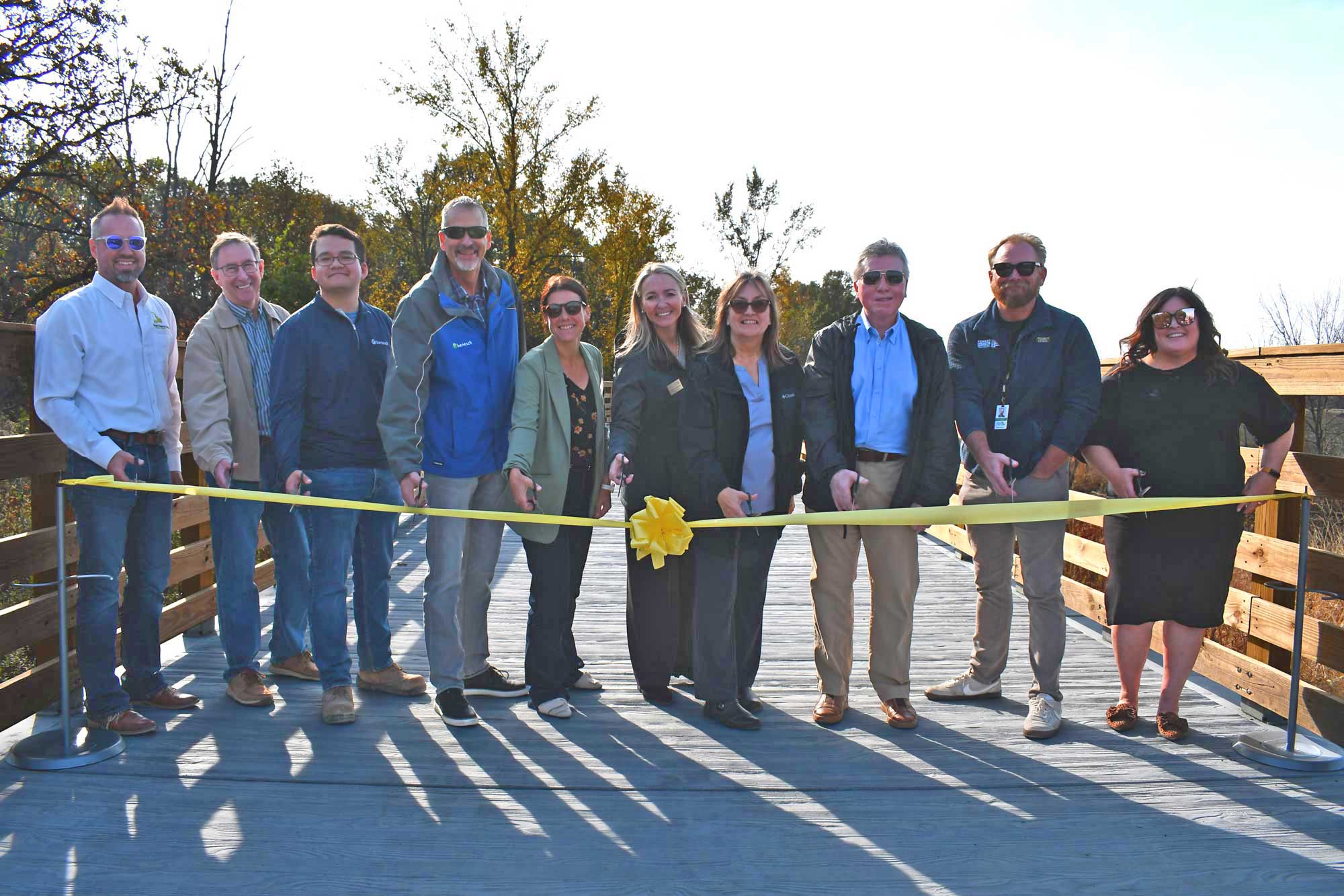 A group of people stand in a line and cut a ribbon to open a new trail.