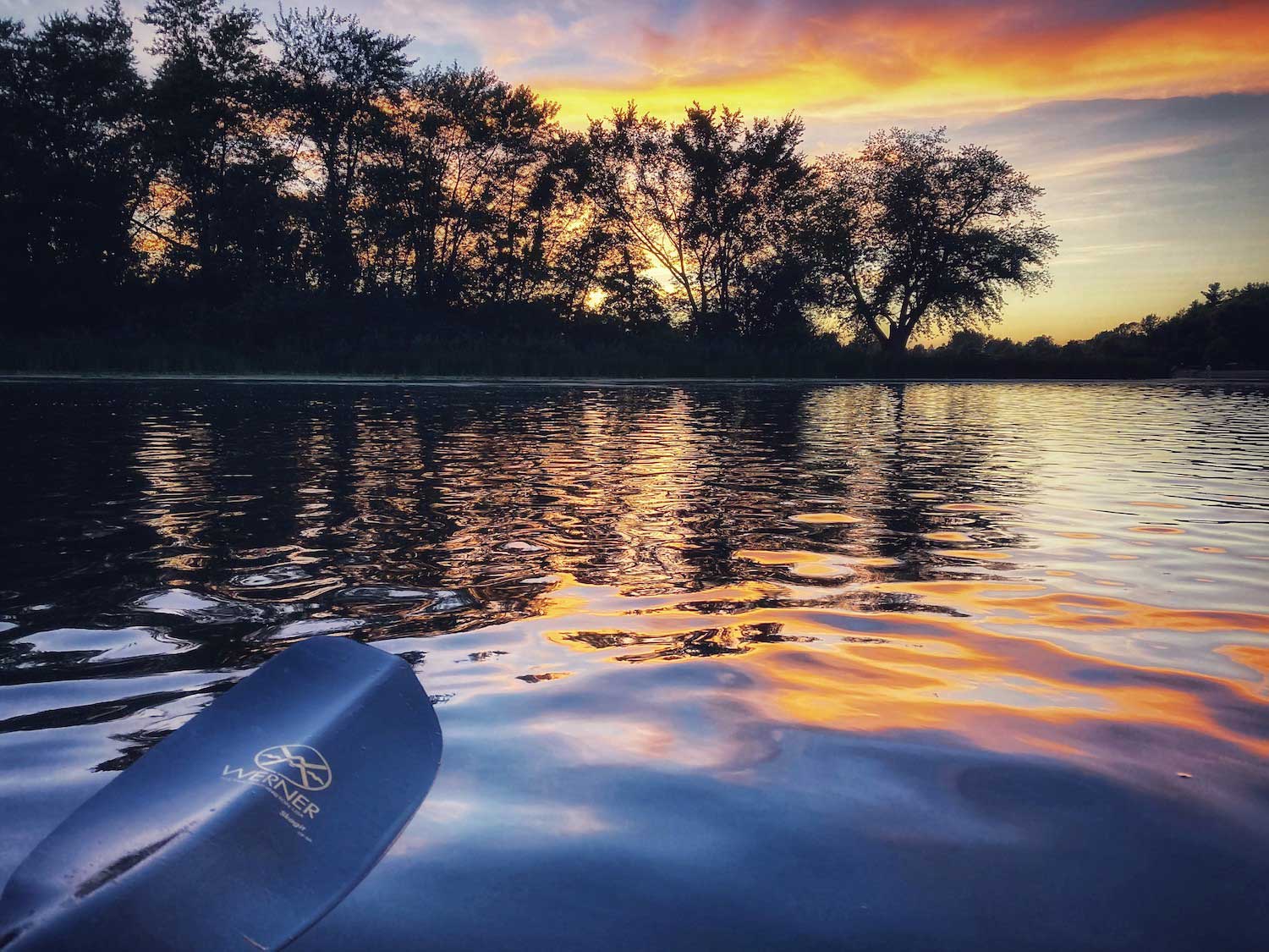 A paddle held over ripped water with the sun setting in the background.