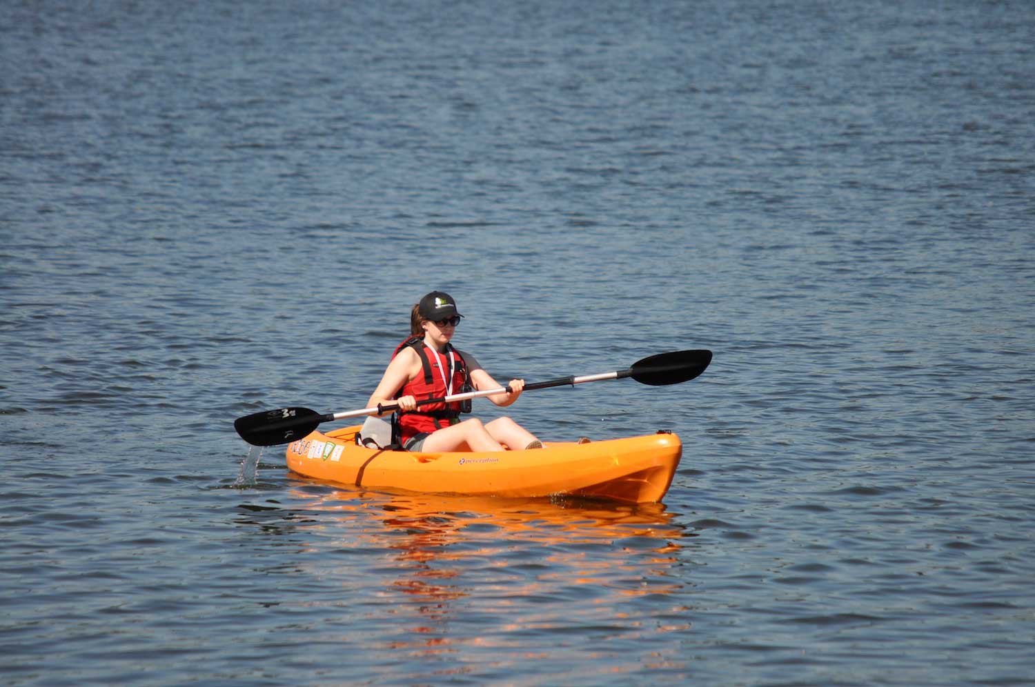 A person holding a paddle while sitting in an orange kayak on a lake.
